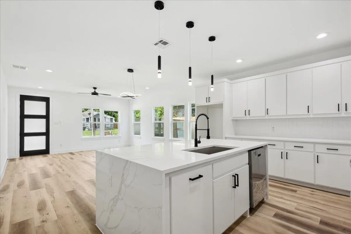 Open-concept layout featuring wood-finish flooring, a kitchen island with a waterfall edge, white shaker cabinetry, a tile backsplash, and contemporary pendant lighting