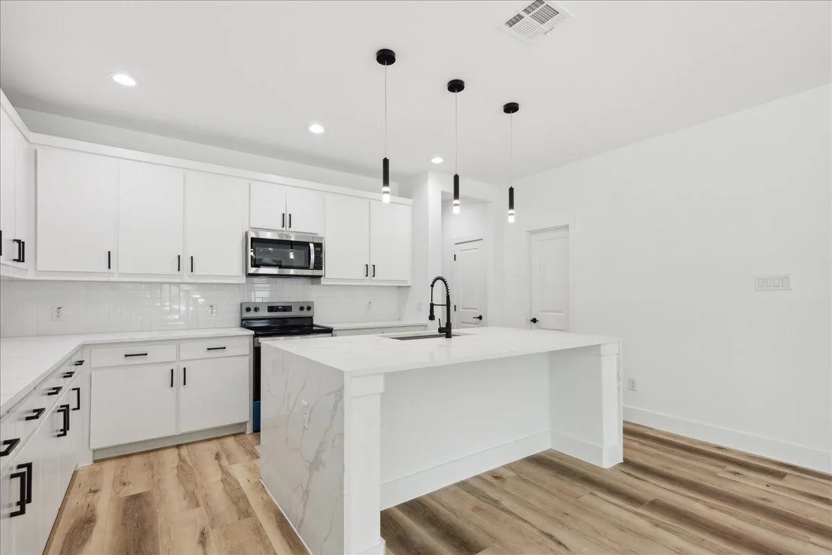 Bright kitchen with extensive white cabinetry, a white subway tile backsplash, stainless steel appliances, and a central island with a waterfall countertop