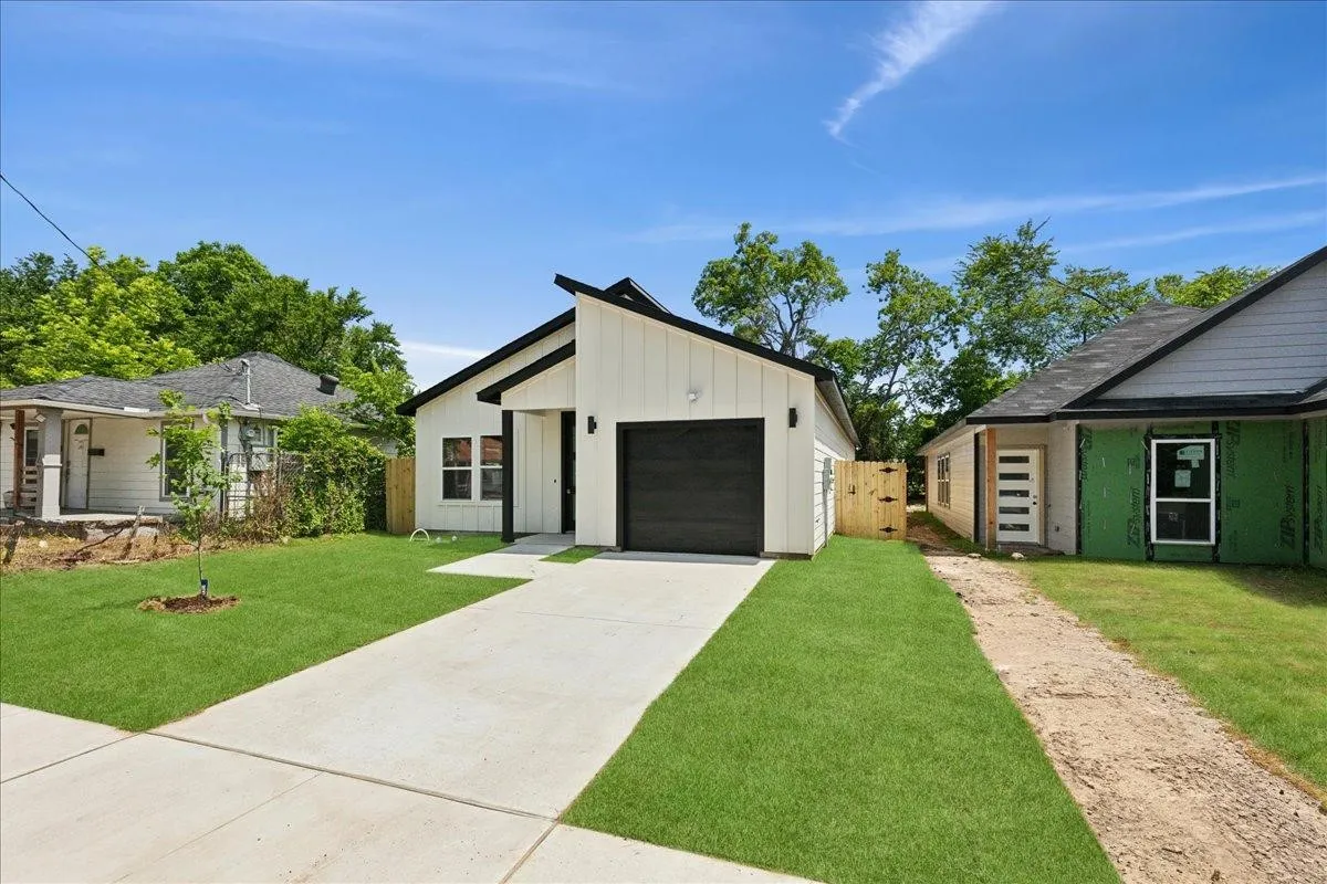 Modern architectural design featuring a white vertical siding exterior, a black garage door, a black framed entry door, and a concrete driveway