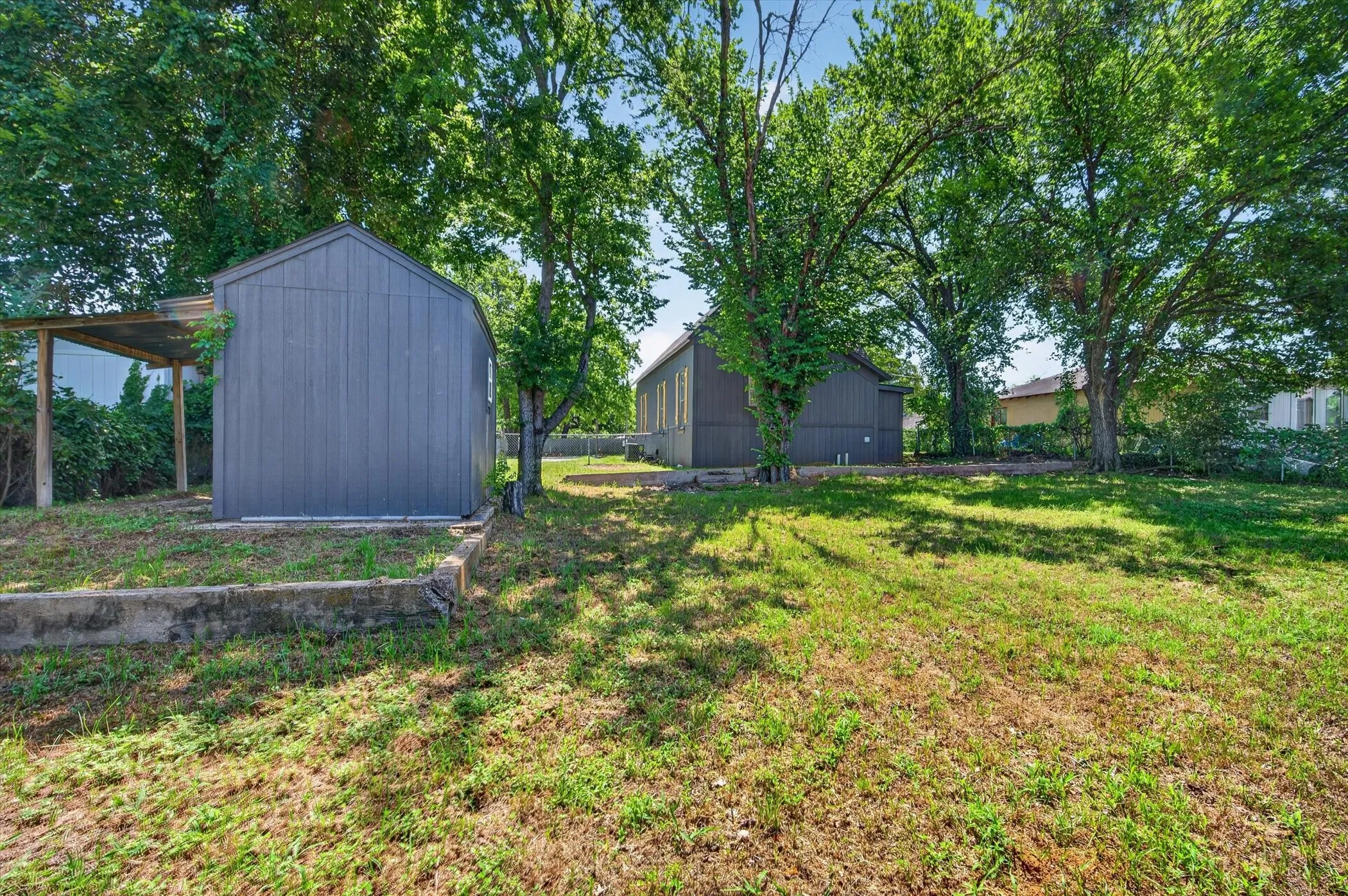 Spacious outdoor area featuring a manicured lawn, established trees, and two storage sheds with durable siding