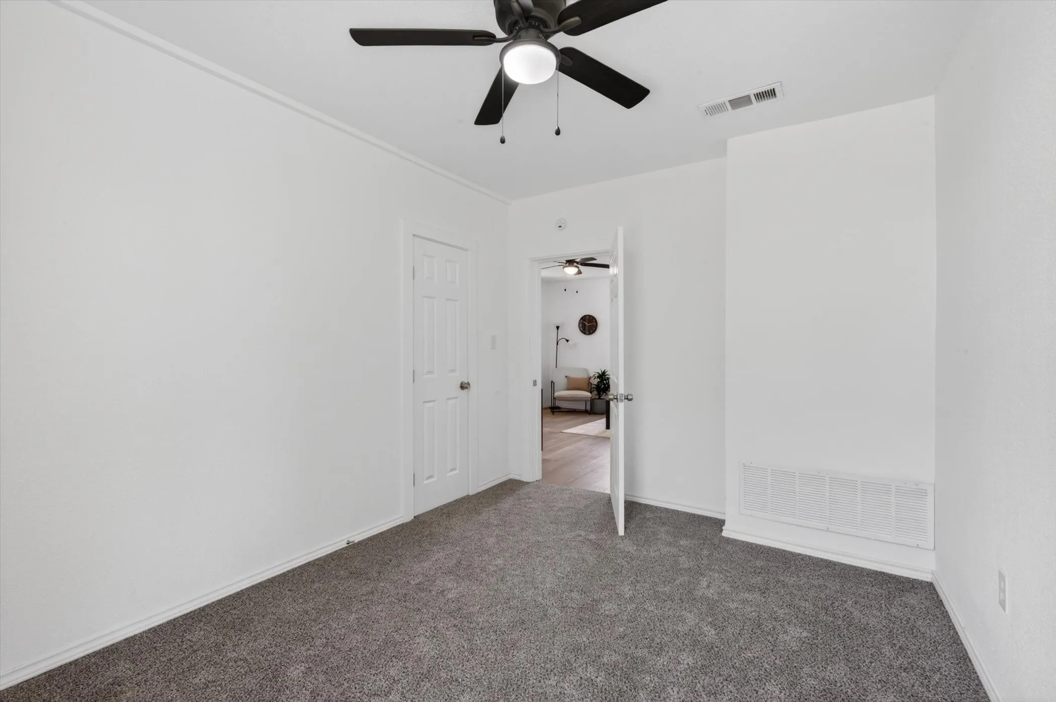 Living area featuring wood-finish flooring, white walls, and a ceiling fan with integrated lighting