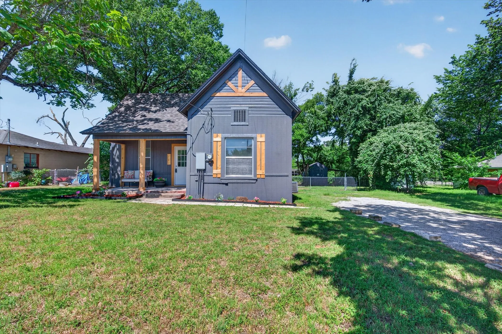 Charming exterior with dark gray siding, a covered front porch with natural wood posts, and a gravel driveway