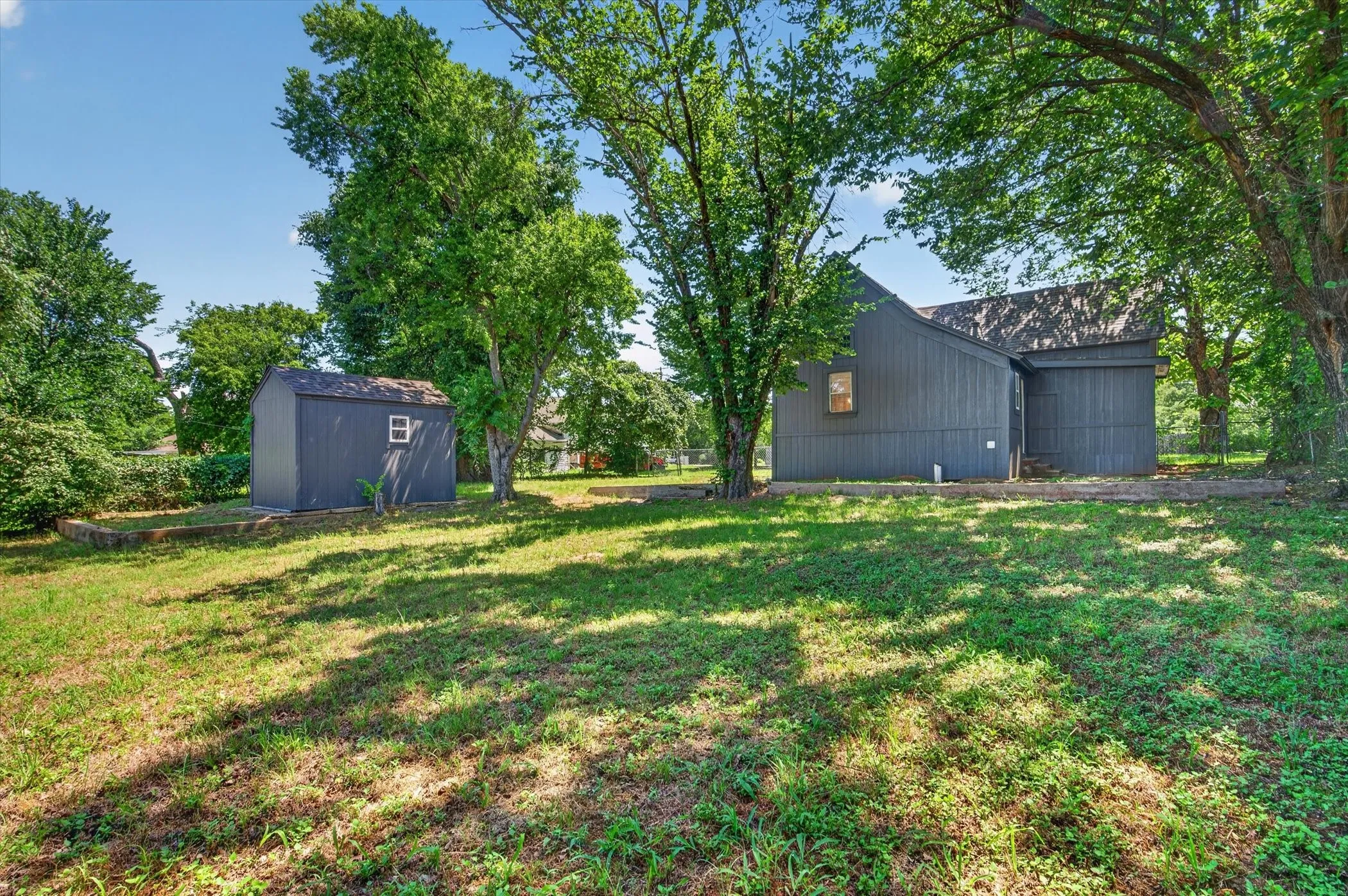 Expansive backyard featuring a manicured lawn, established trees, and a detached storage shed