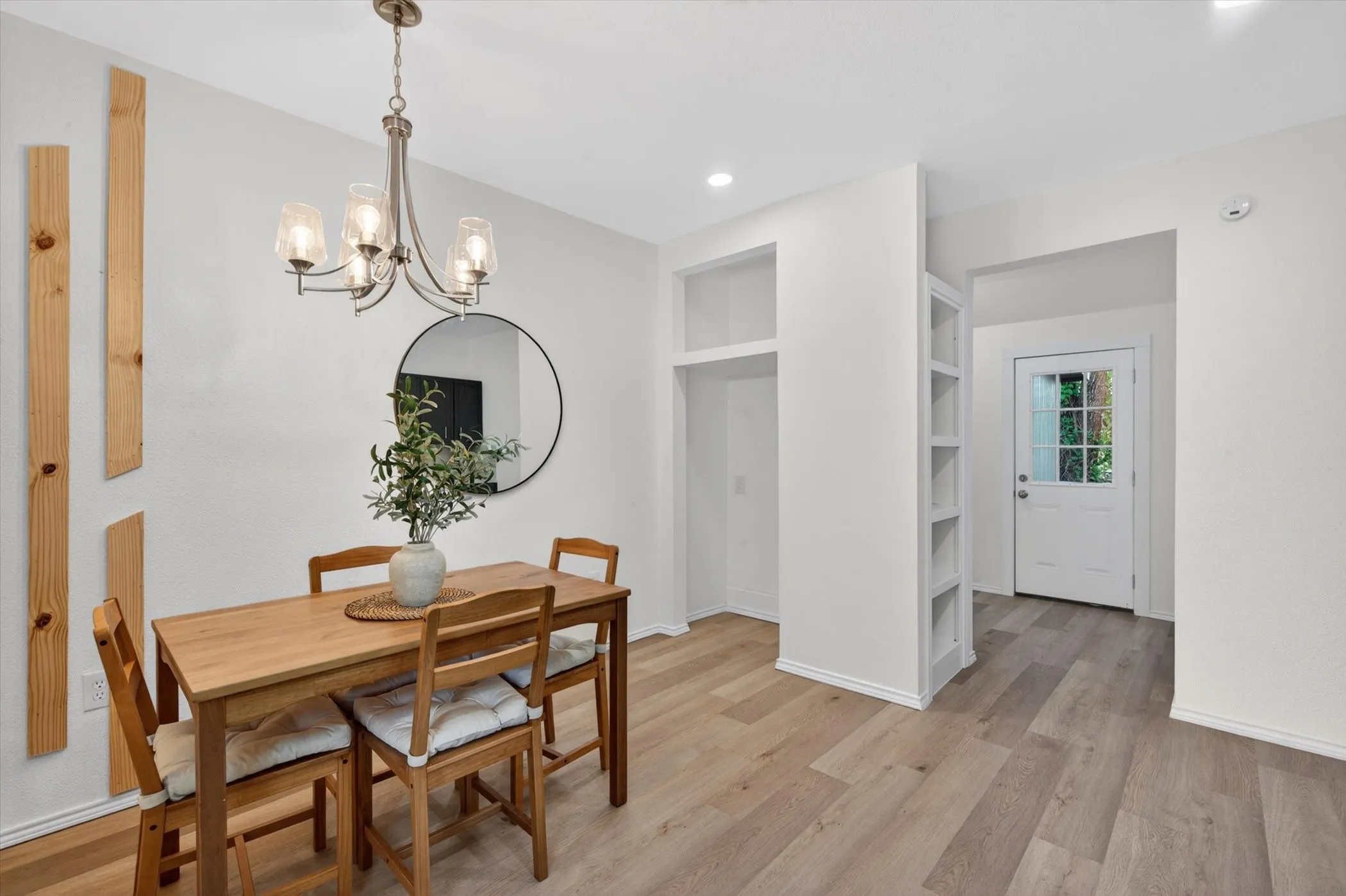 Open-concept dining area featuring wood-finish flooring, a contemporary chandelier, built-in shelving, recessed lighting, and a white paneled door with glass inserts