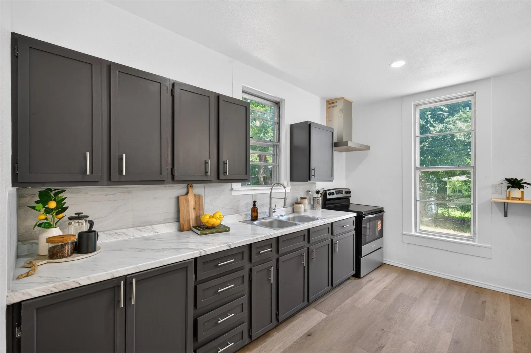 Kitchen featuring dark cabinetry, light-toned countertops, stainless steel appliances, a double basin sink, and wood-finish flooring