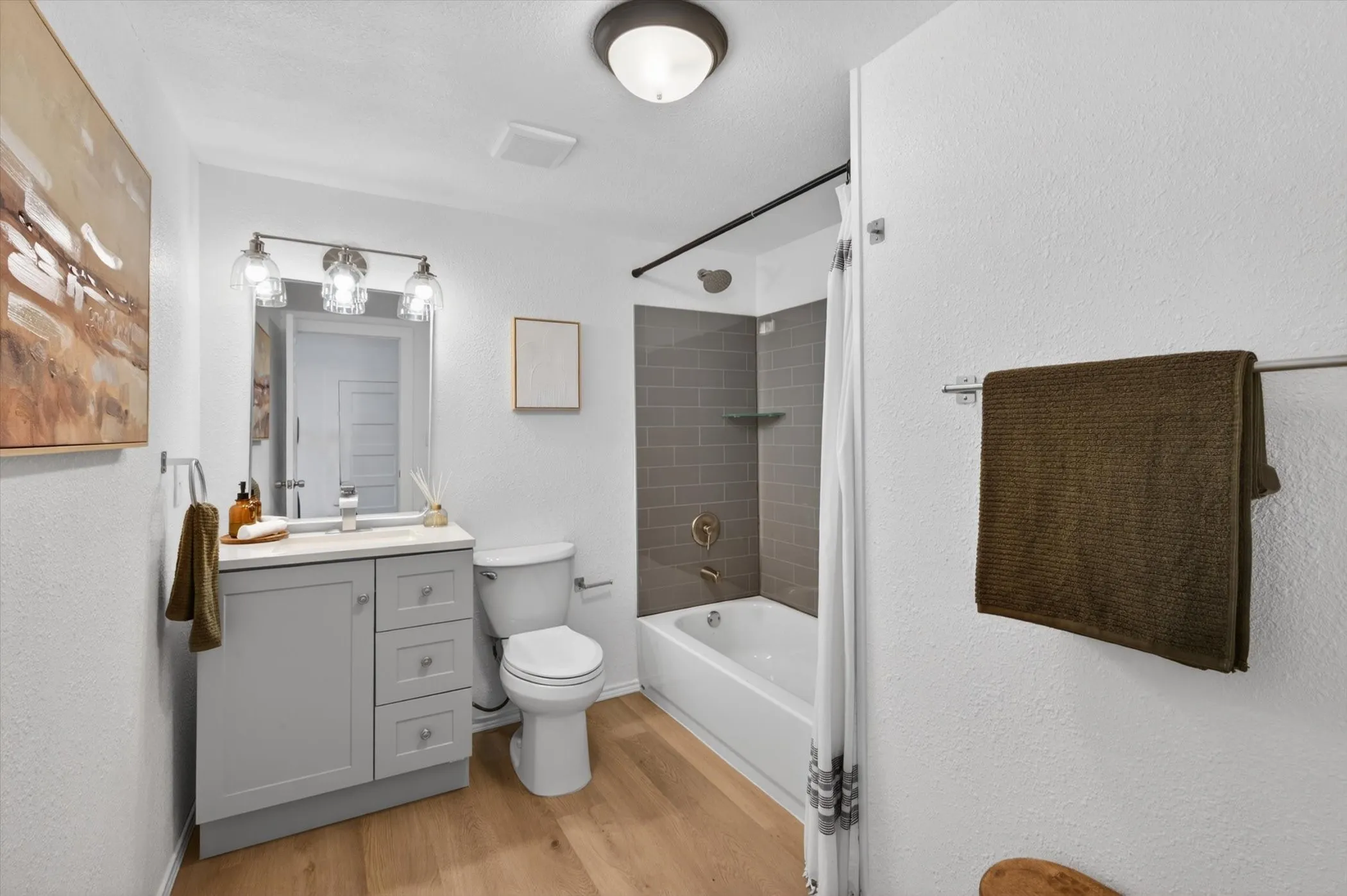 Bathroom featuring wood-finish flooring, a light gray vanity with a countertop sink, a full-size tub, and subway-tiled shower walls with built-in shelving