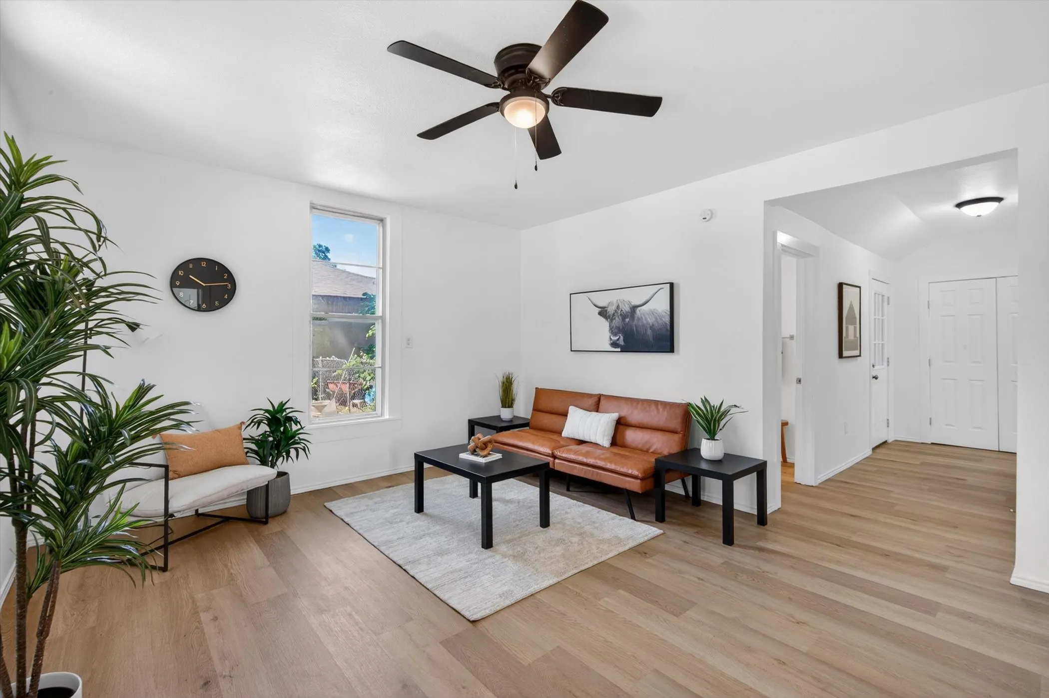 Living area featuring wood-finish flooring, white walls, and a ceiling fan with integrated lighting