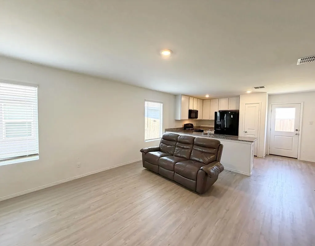 Open-concept living area with wood-finish flooring, recessed lighting, and kitchen with light cabinetry and dark appliances