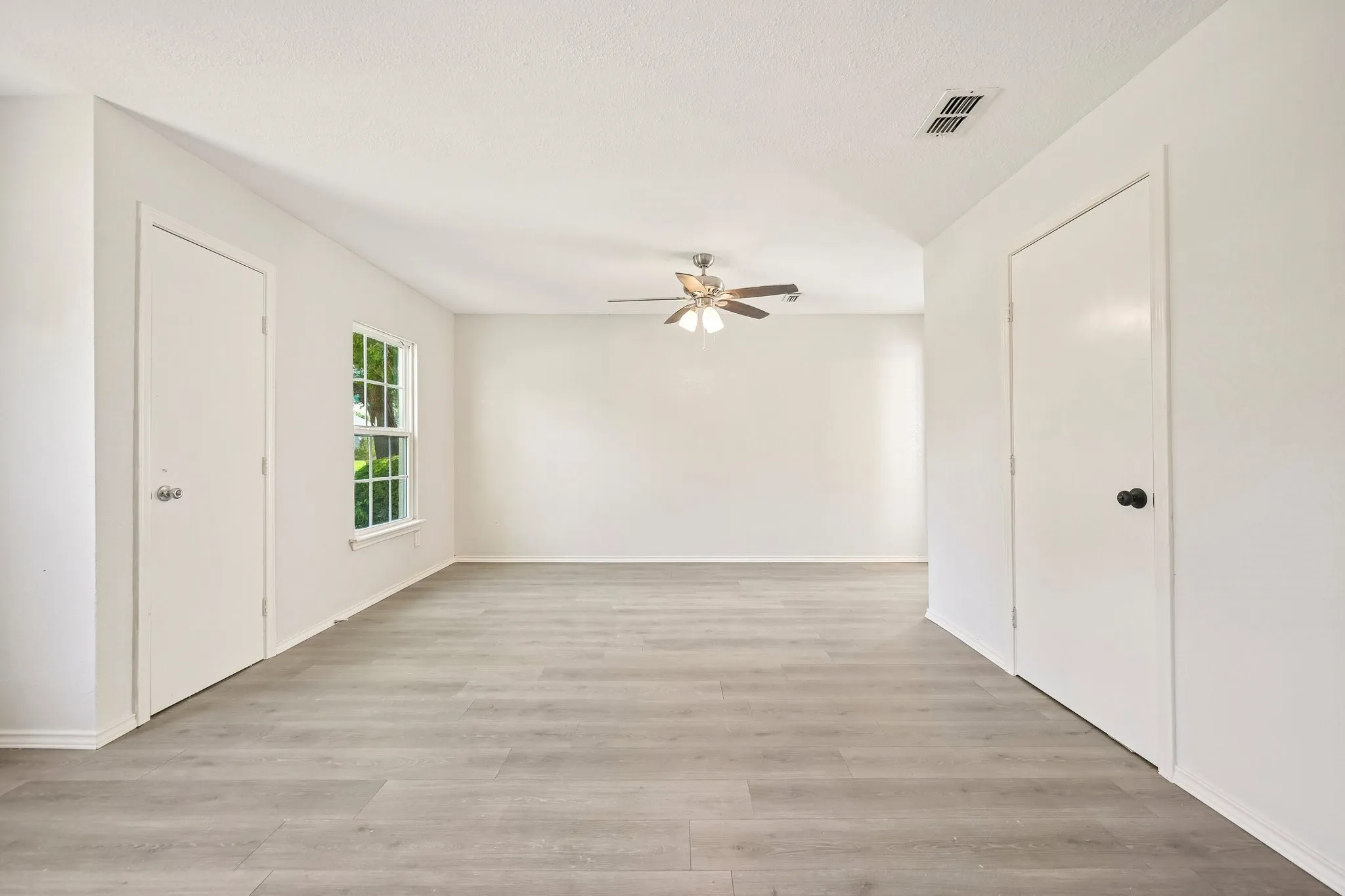 Spacious room featuring wood-finish flooring, a ceiling fan, and a double-hung window