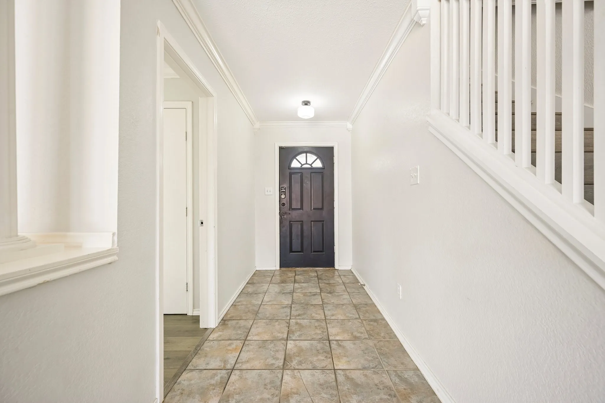 Tiled flooring, white wall paint, crown molding, white stair railing, and a dark entry door with decorative glass