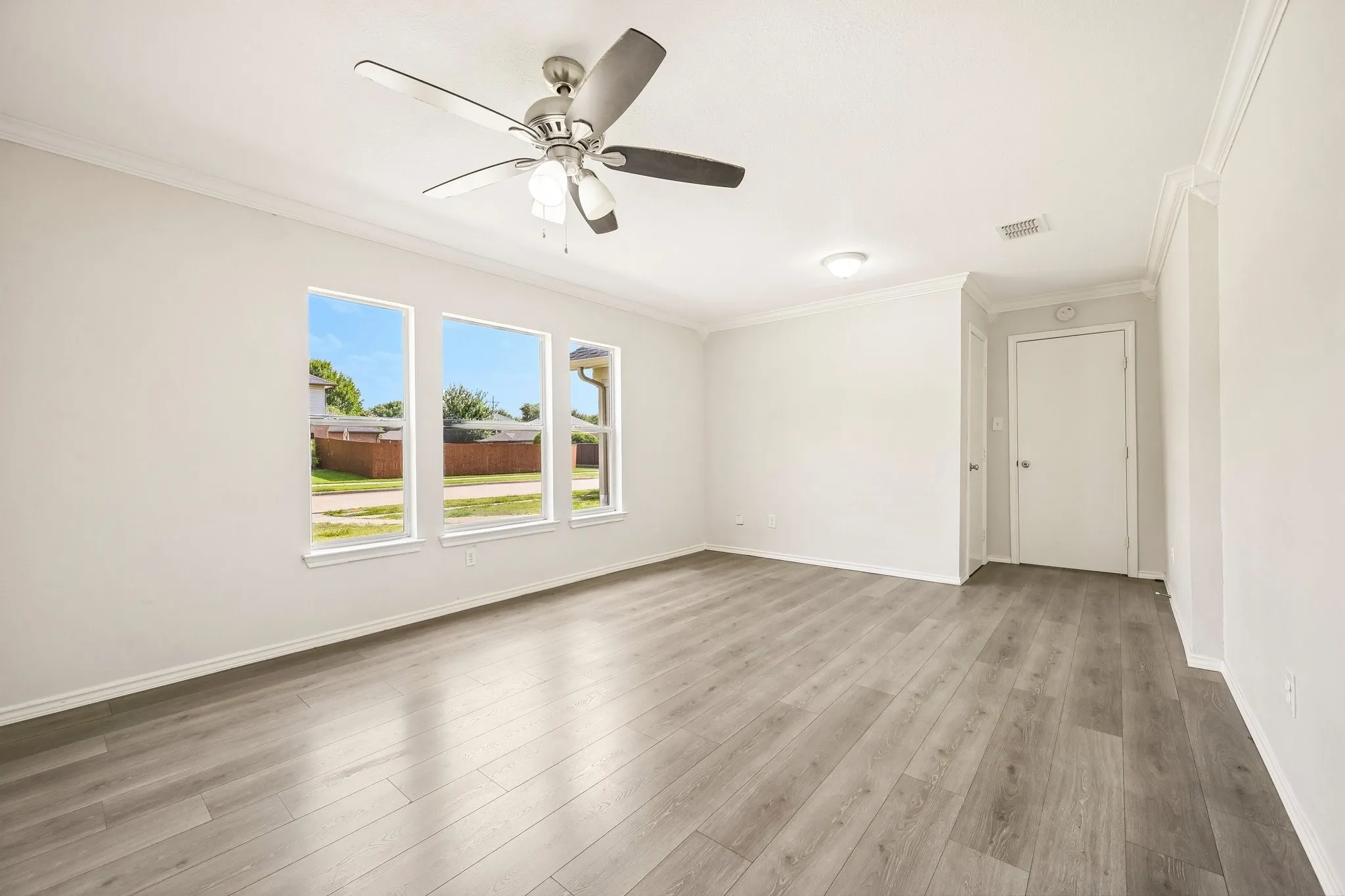 Light wood-finish flooring, three large windows, ceiling fan, crown molding, and recessed lighting