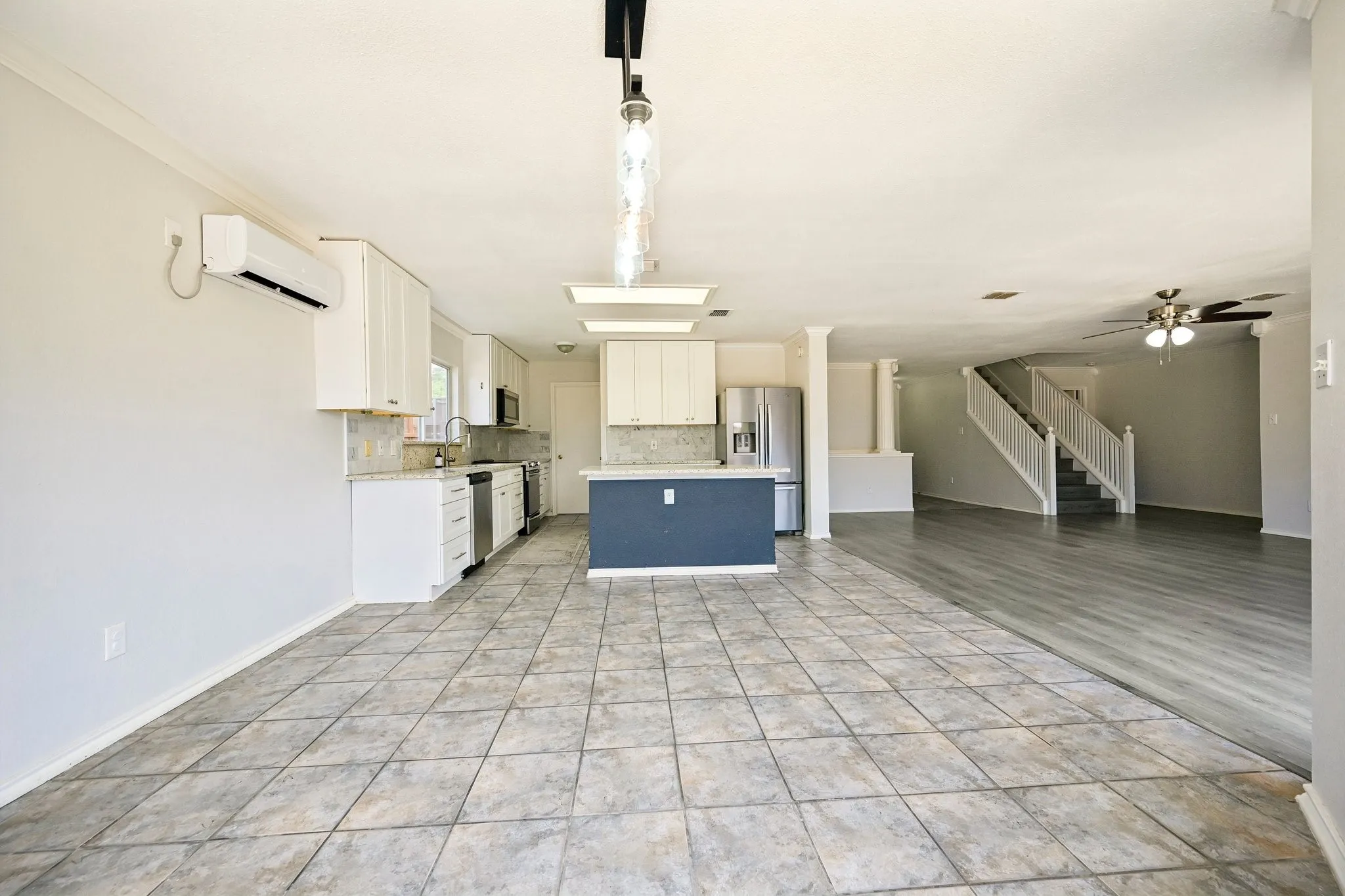 Open-concept living space with tile and wood-finish flooring, a kitchen island, and white cabinetry