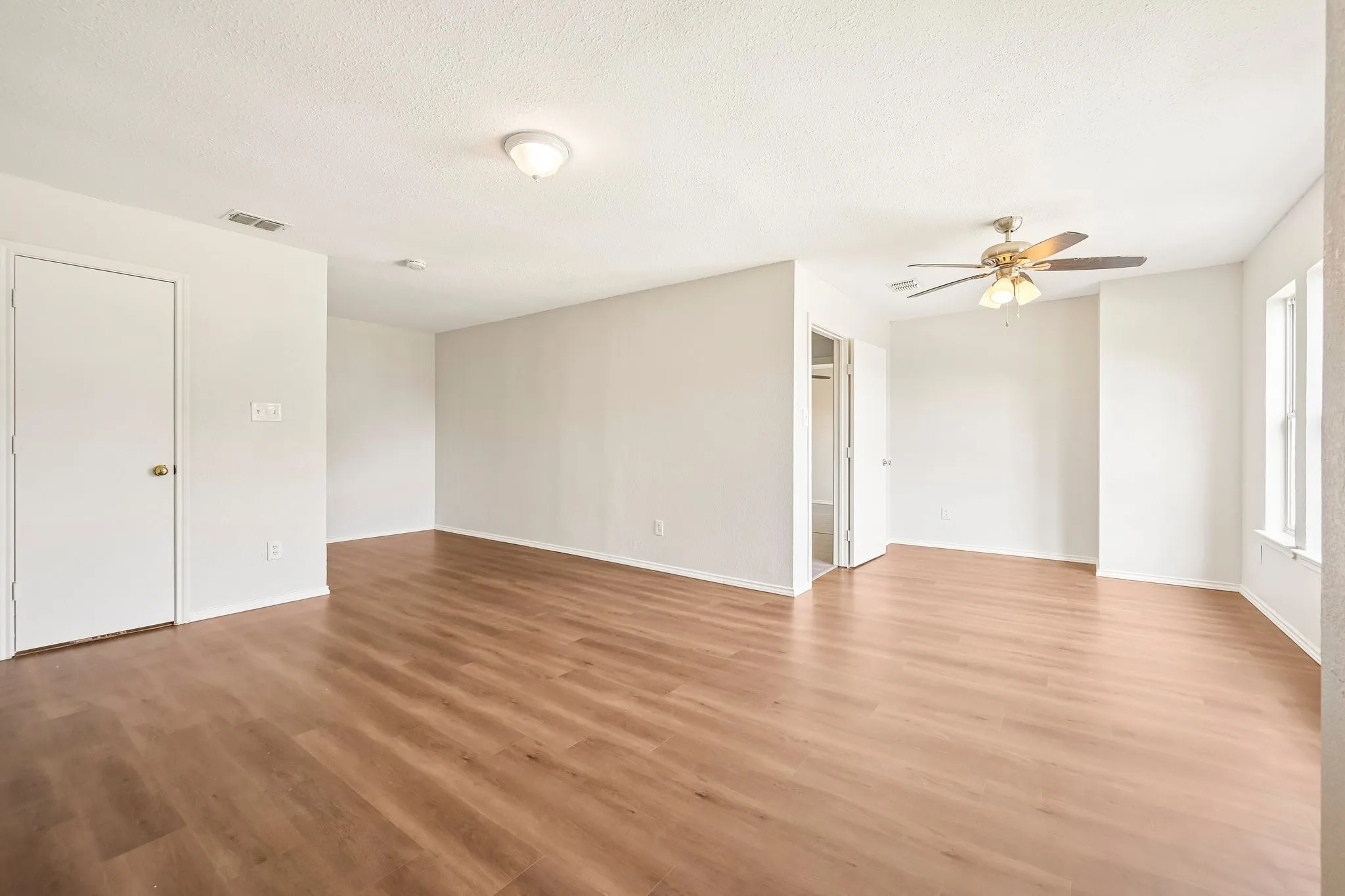 Spacious interior featuring wood-finish flooring, white walls, ceiling fan, and ample natural light from multiple windows