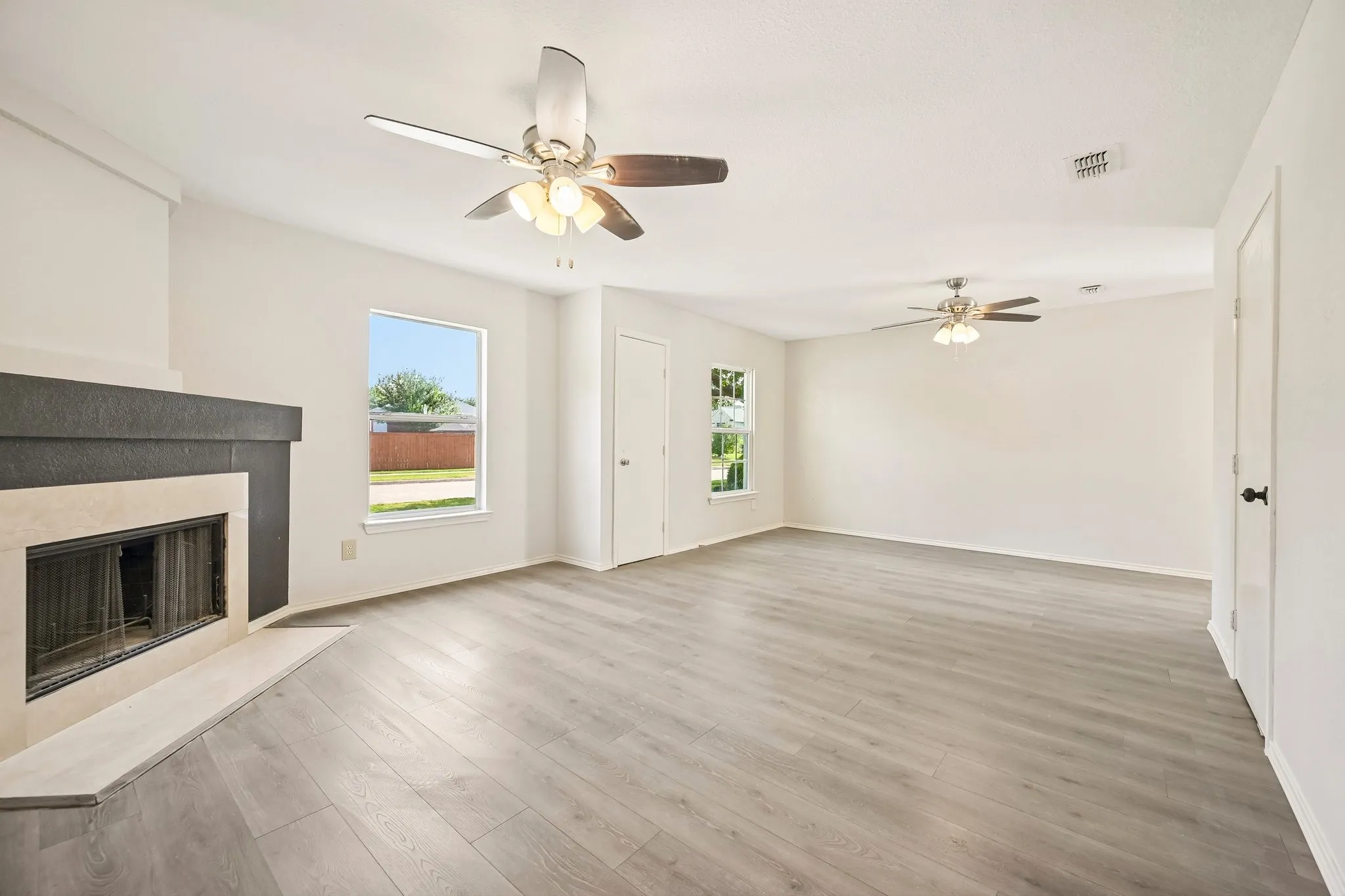 Spacious living area featuring wood-finish flooring, a fireplace with a stone surround, and multiple ceiling fans