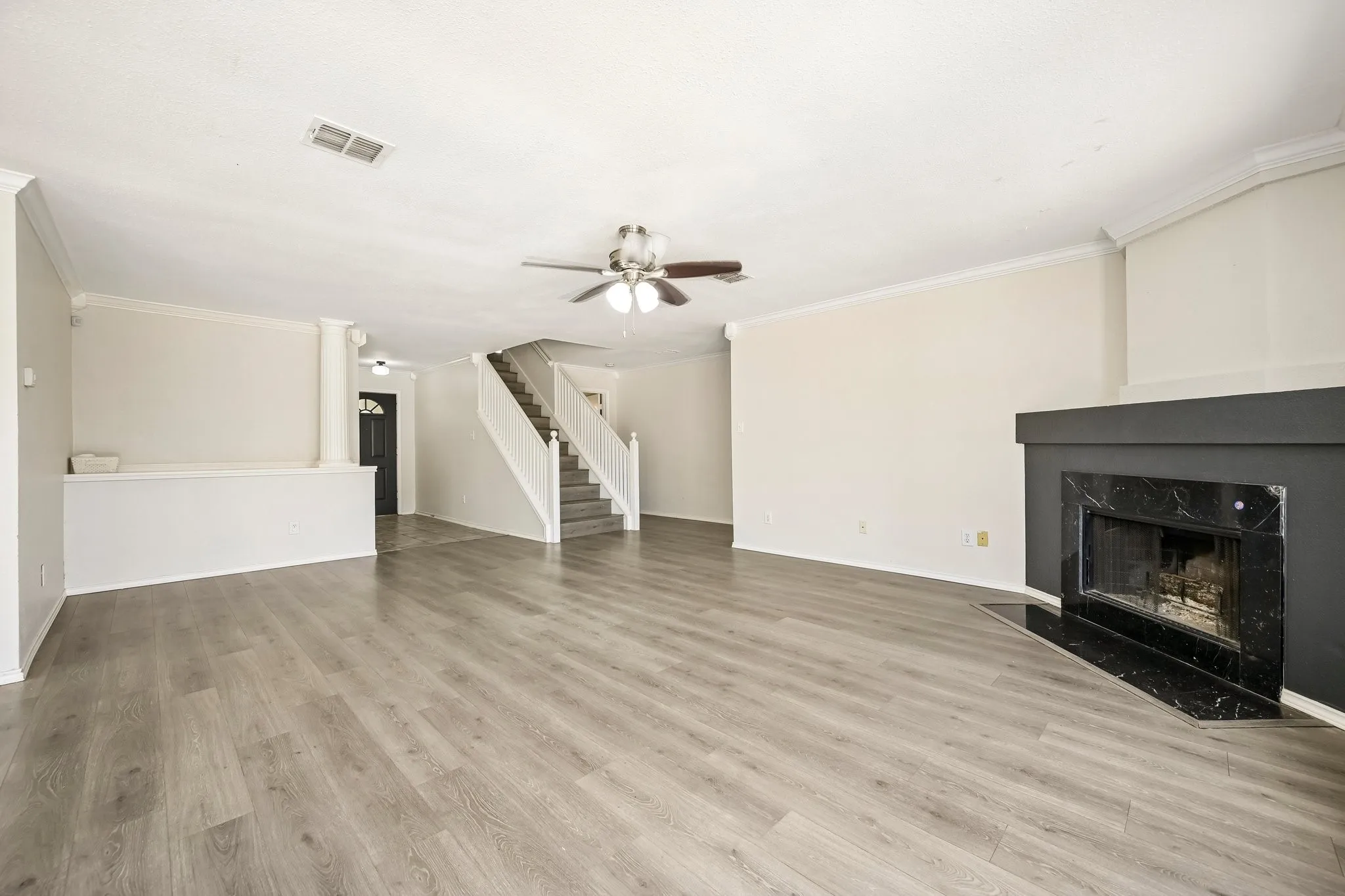 Spacious living area featuring wood-finish flooring, a ceiling fan, crown molding, and a fireplace with a black surround