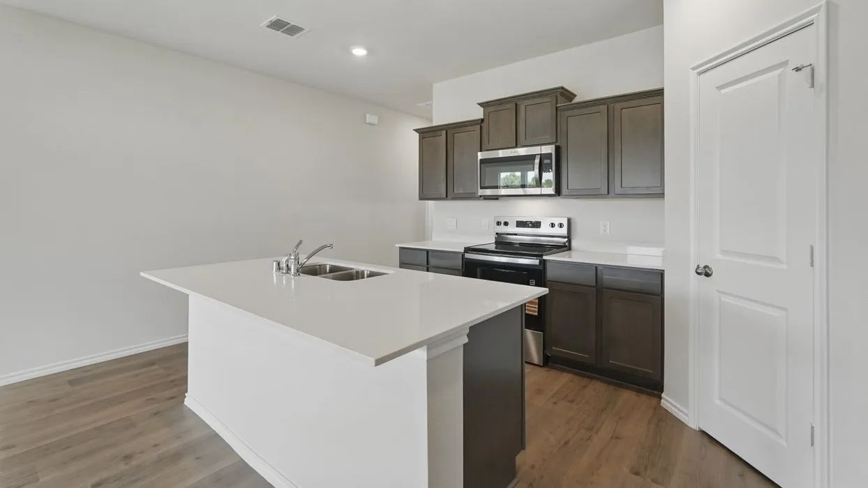 Kitchen featuring an island with an undermount dual-basin sink and stainless steel faucet, dark wood-finish cabinetry, stainless steel appliances, and light-toned countertops