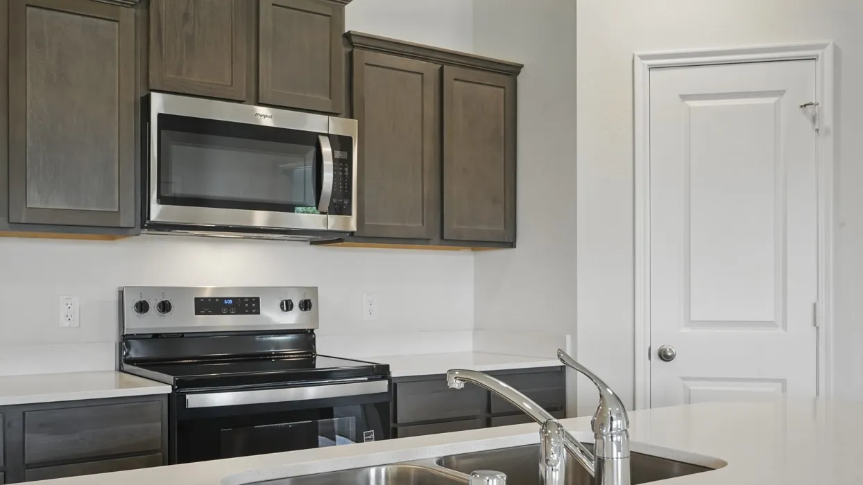 Stainless steel appliance suite, dark wood-finish cabinetry, light countertops, and double basin sink with chrome faucet