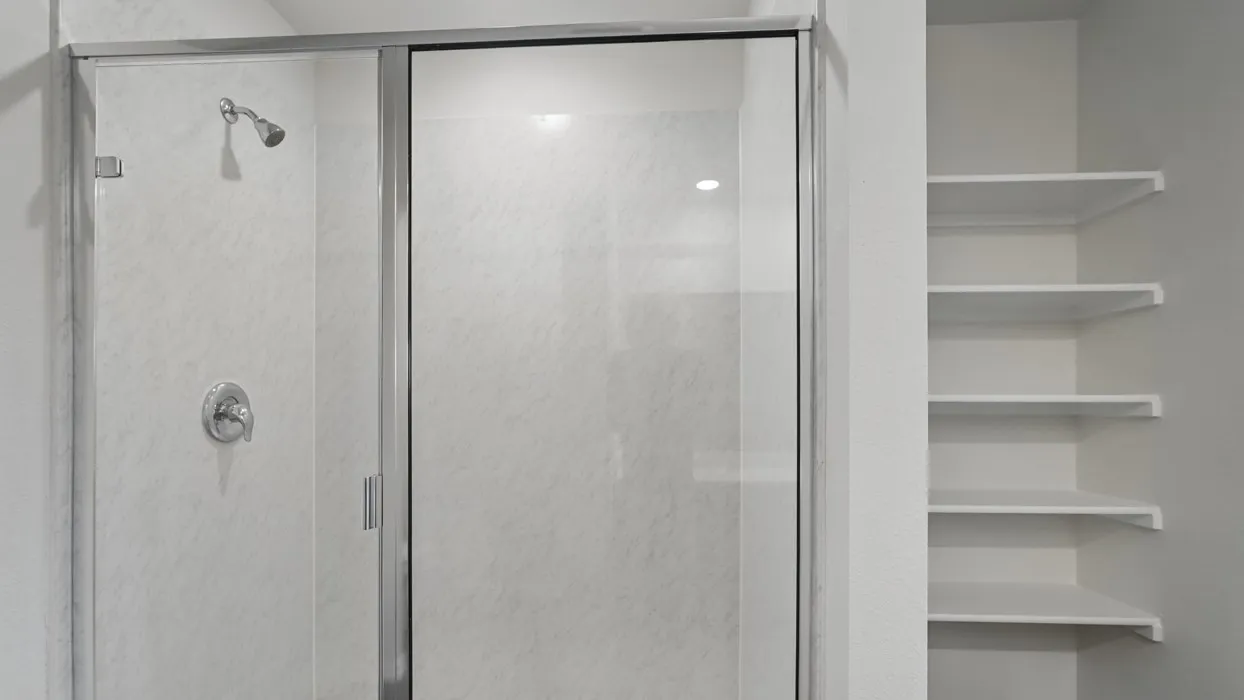 Shower enclosure with clear glass door, chrome fixtures, and integrated wall shelving