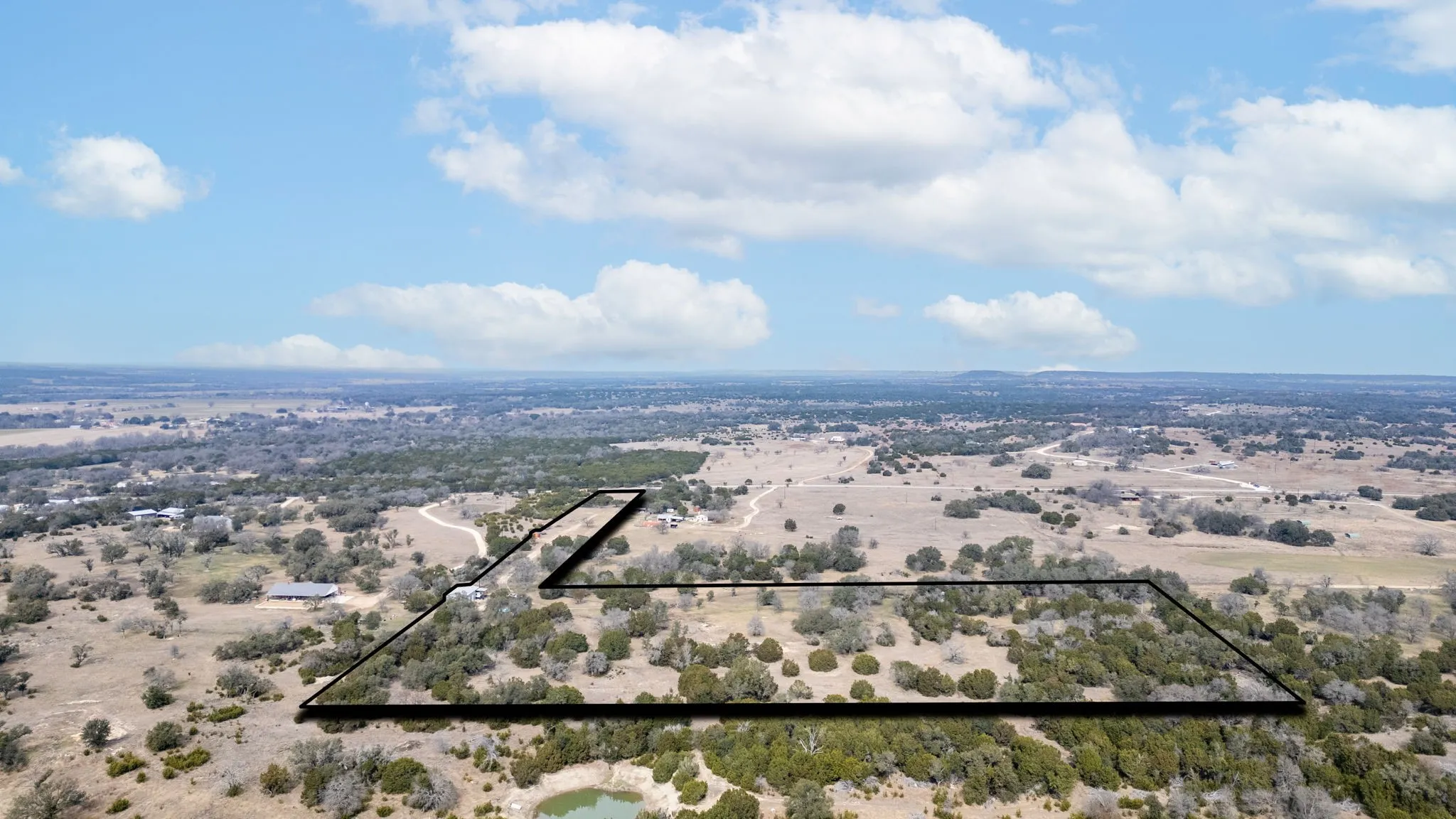 Expansive land parcel with varied topography, featuring a natural water body and scattered mature trees