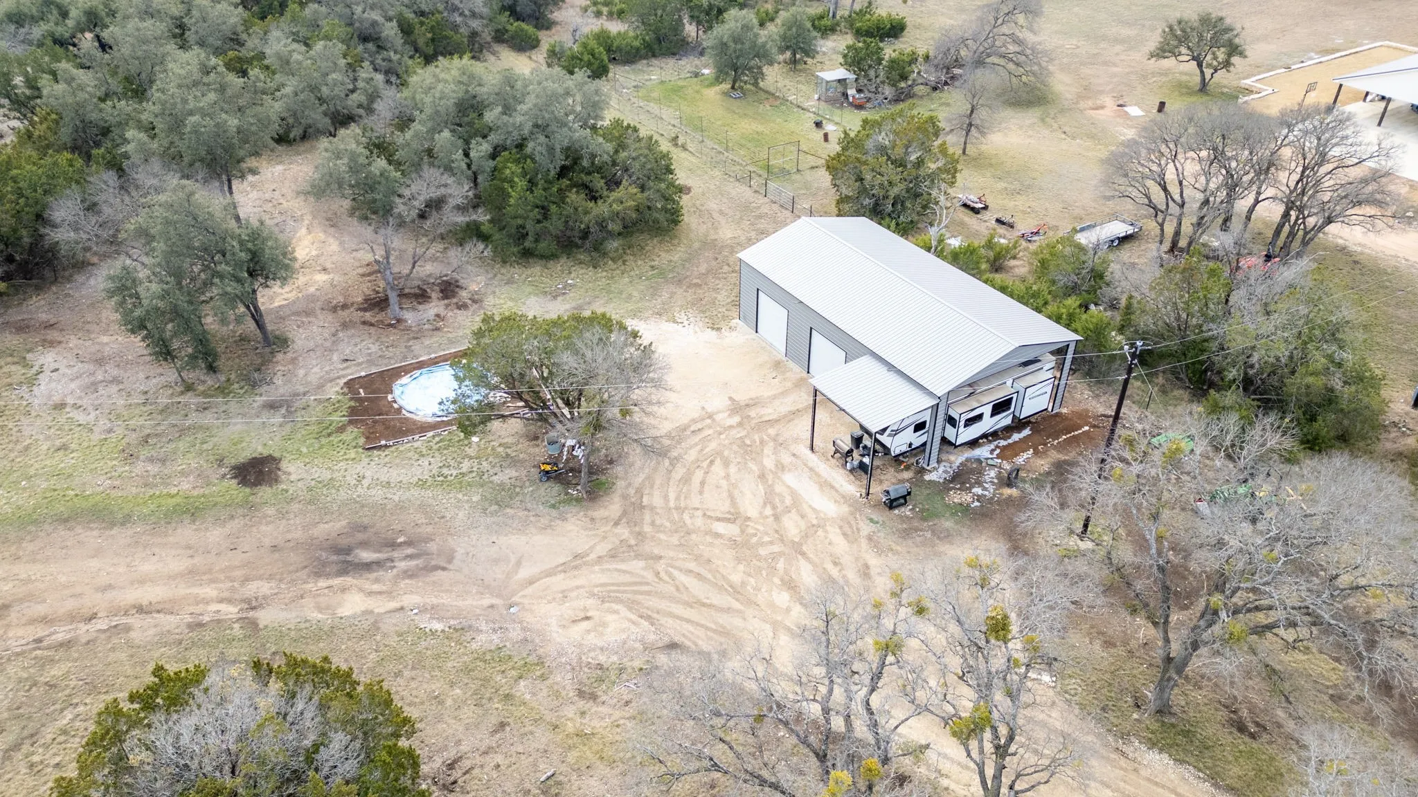Metal-clad structure with multiple garage bays, covered outdoor parking area, and an in-ground swimming pool