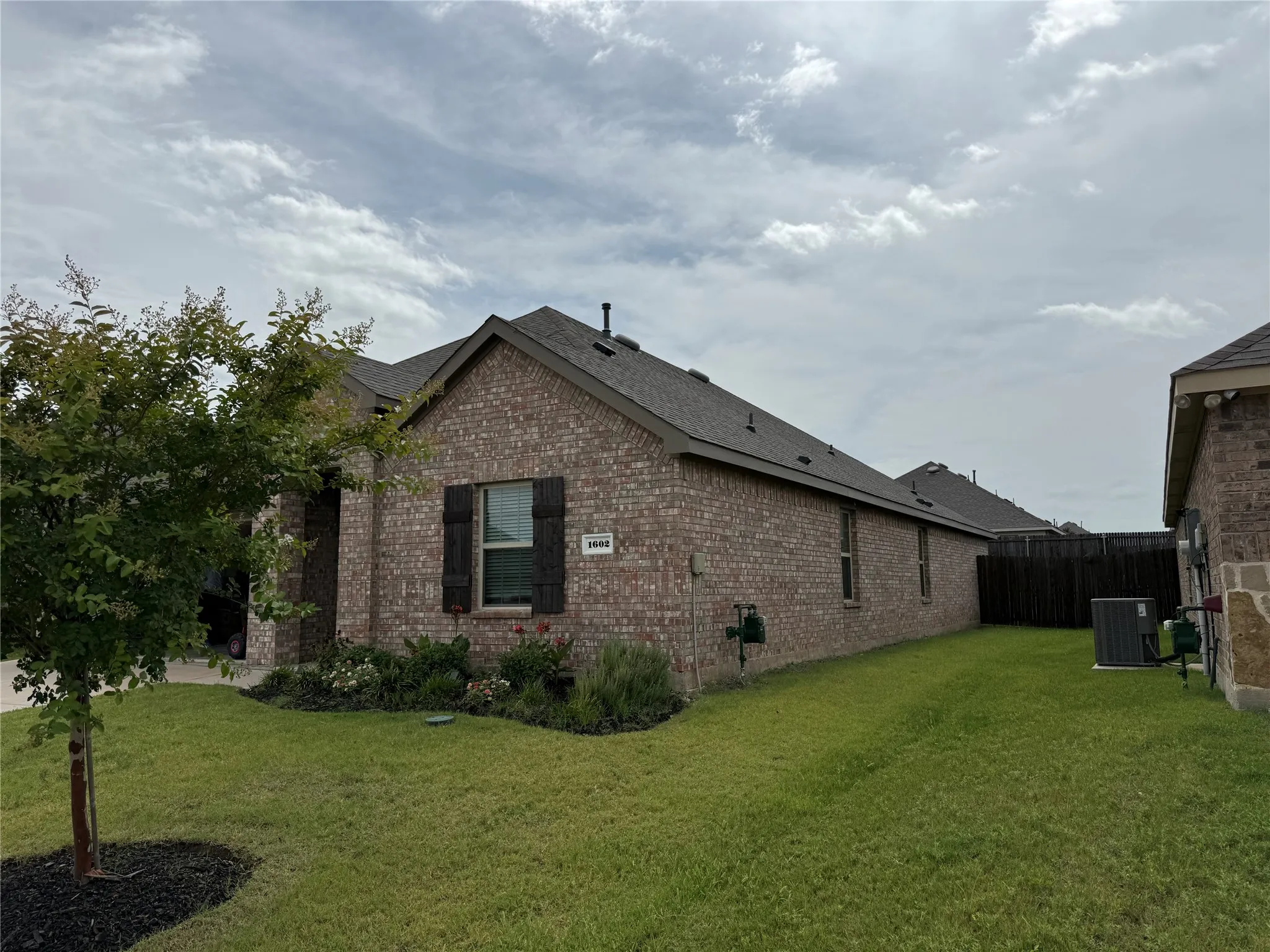 Brick exterior with dark shutters, gabled roofline, and attached fencing