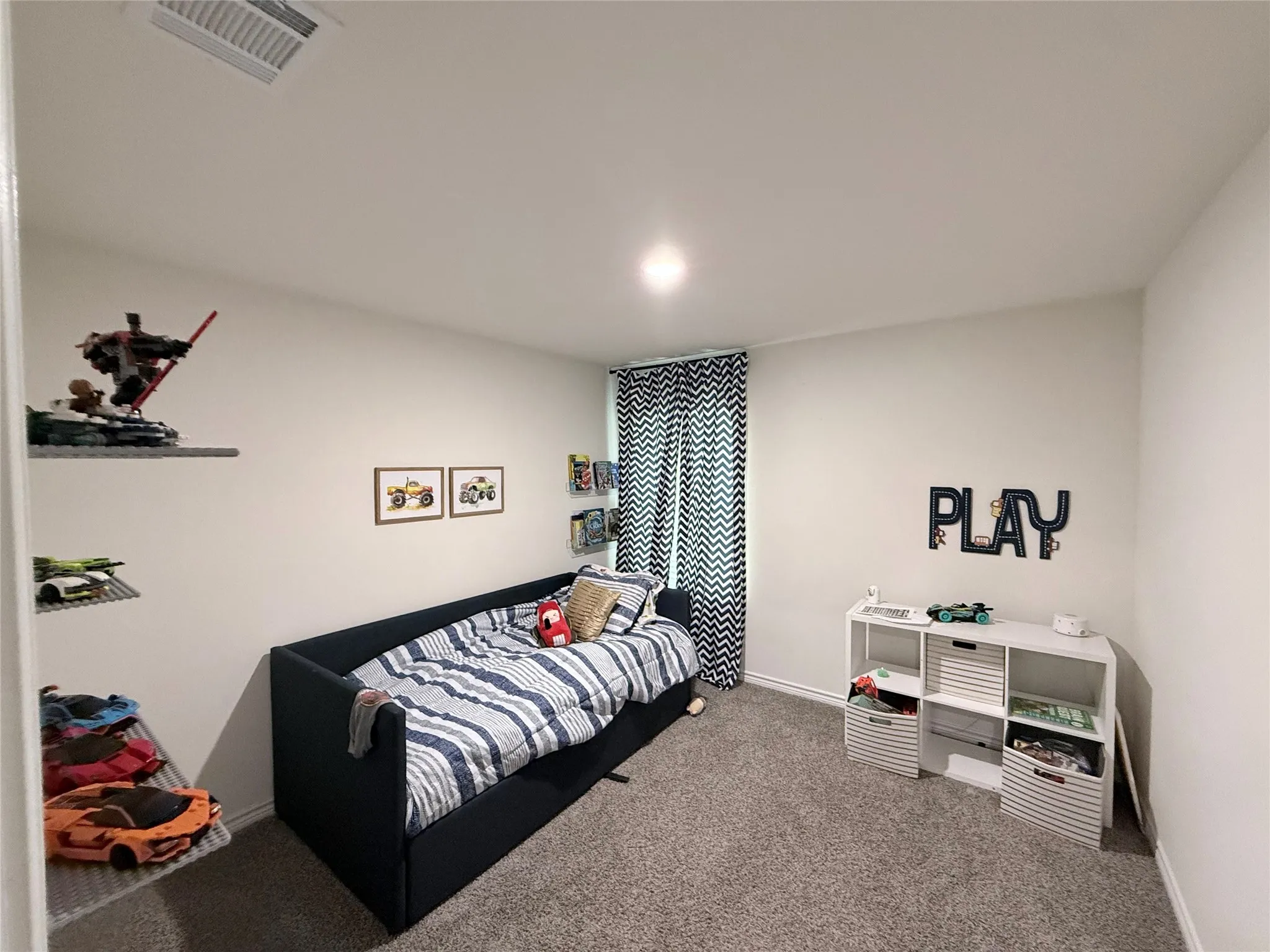 Recessed ceiling lighting, wall-mounted shelving, white wall paint, patterned window treatments, and gray carpeting