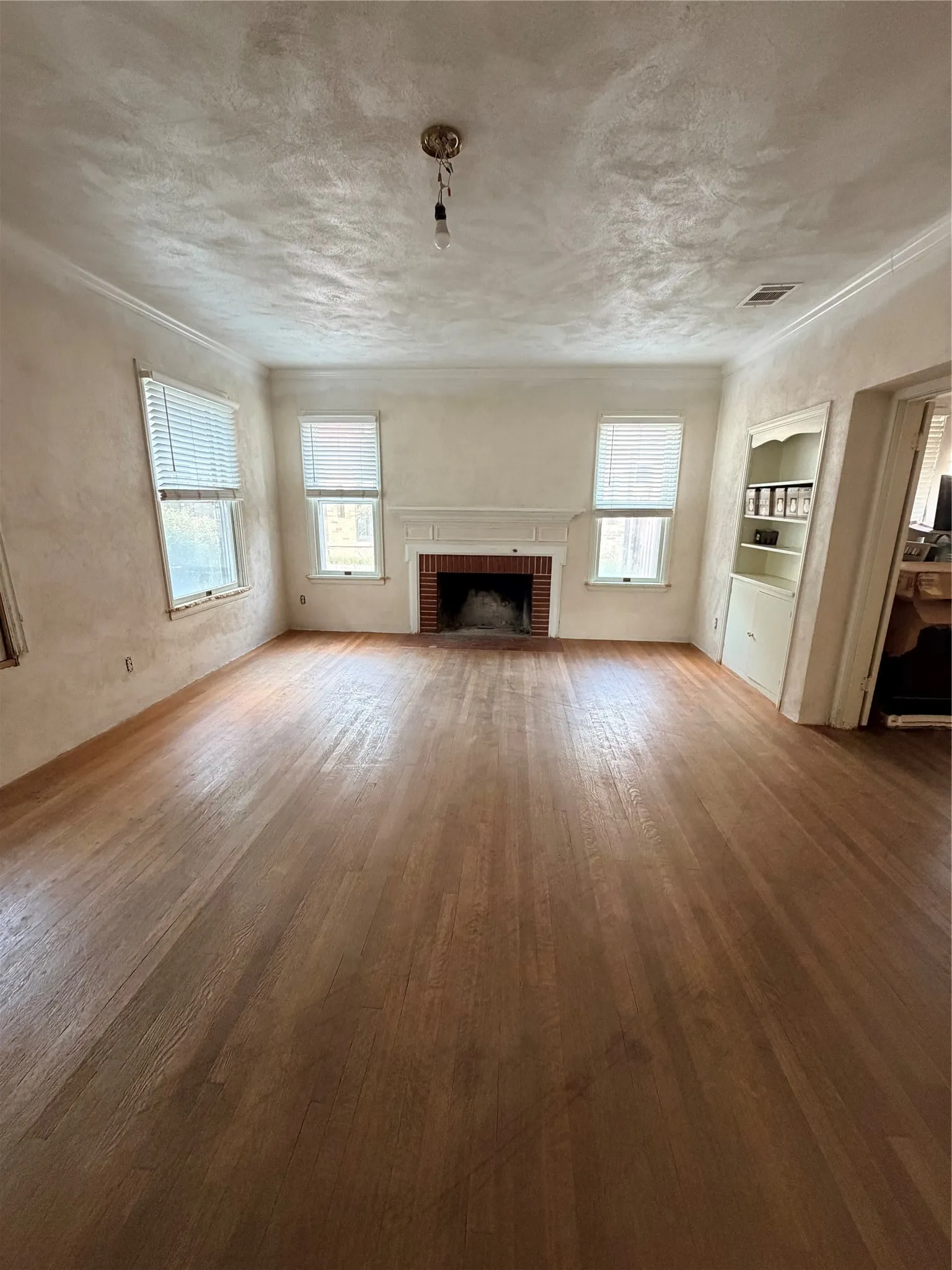 Spacious living room featuring hardwood flooring throughout, a wood-burning fireplace with surround, three large windows with natural light, built-in shelving, and a coffered ceiling detail