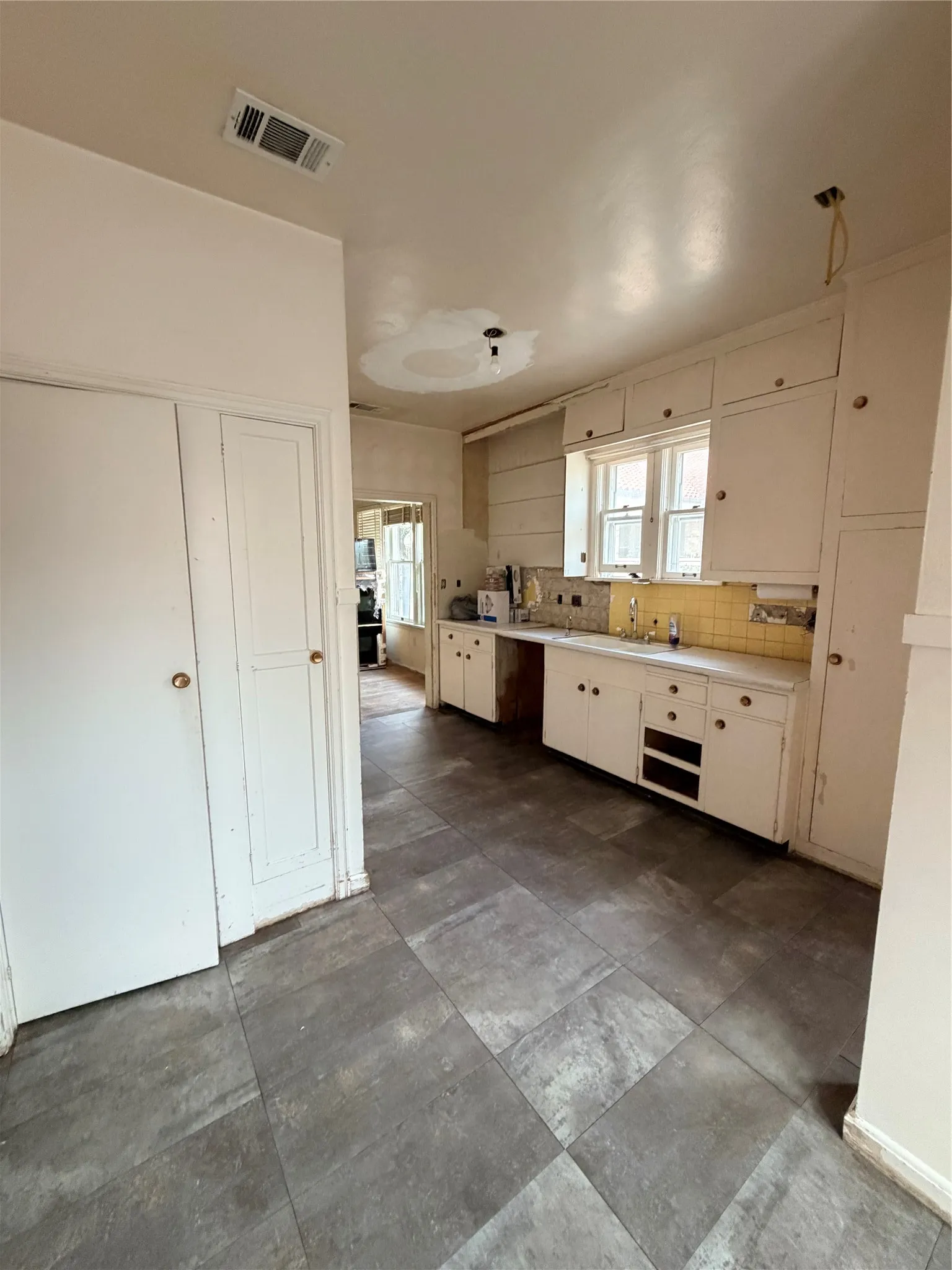 Kitchen area featuring a window, white cabinetry, a sink, and a yellow tiled backsplash