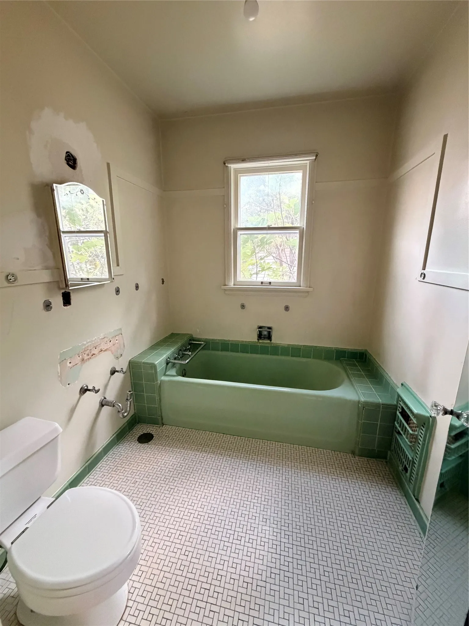 Recessed bathtub with green tile surround, white toilet, and geometric pattern floor tiling