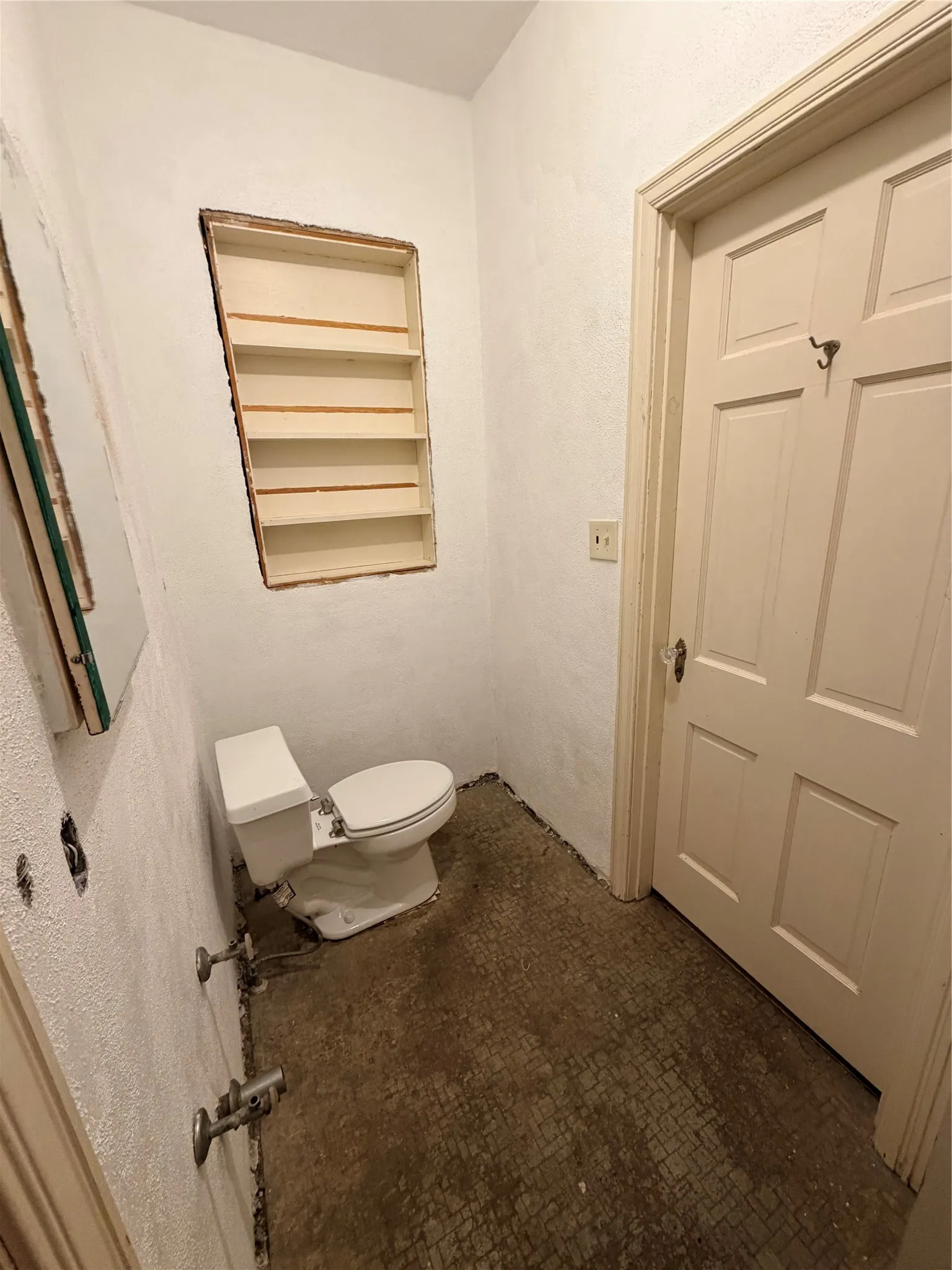 Built-in wall shelving, paneled door with trim, wall-mounted plumbing fixtures, and a classic white toilet