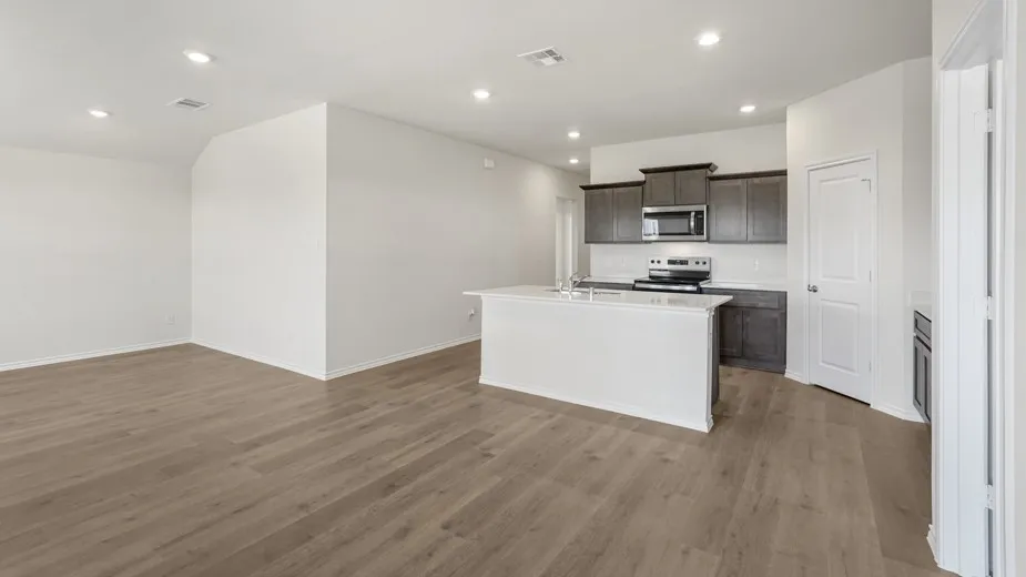 Expansive wood-finish flooring throughout, recessed lighting, kitchen island with built-in sink, dark wood cabinetry, and stainless steel appliances