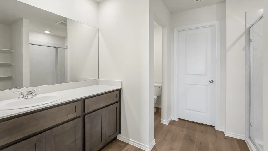 Single vanity with an integrated sink, polished chrome faucet, wood-finish cabinetry, and a large wall mirror