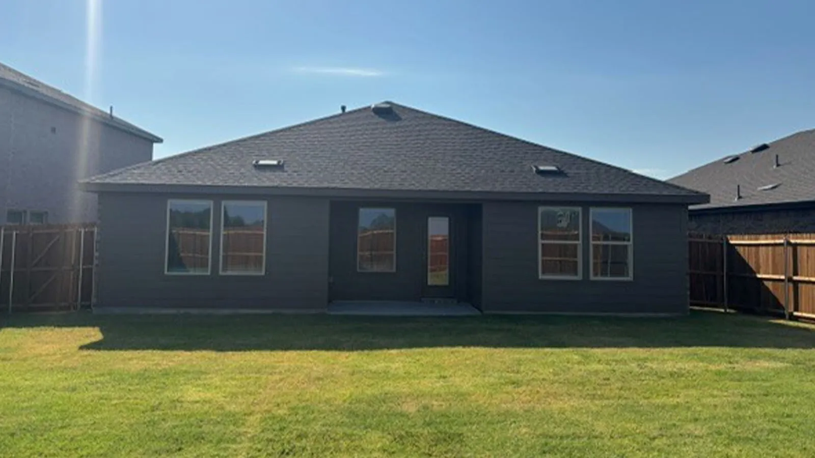 Expansive green lawn, dark gray exterior siding, multiple windows, skylights, and a concrete patio