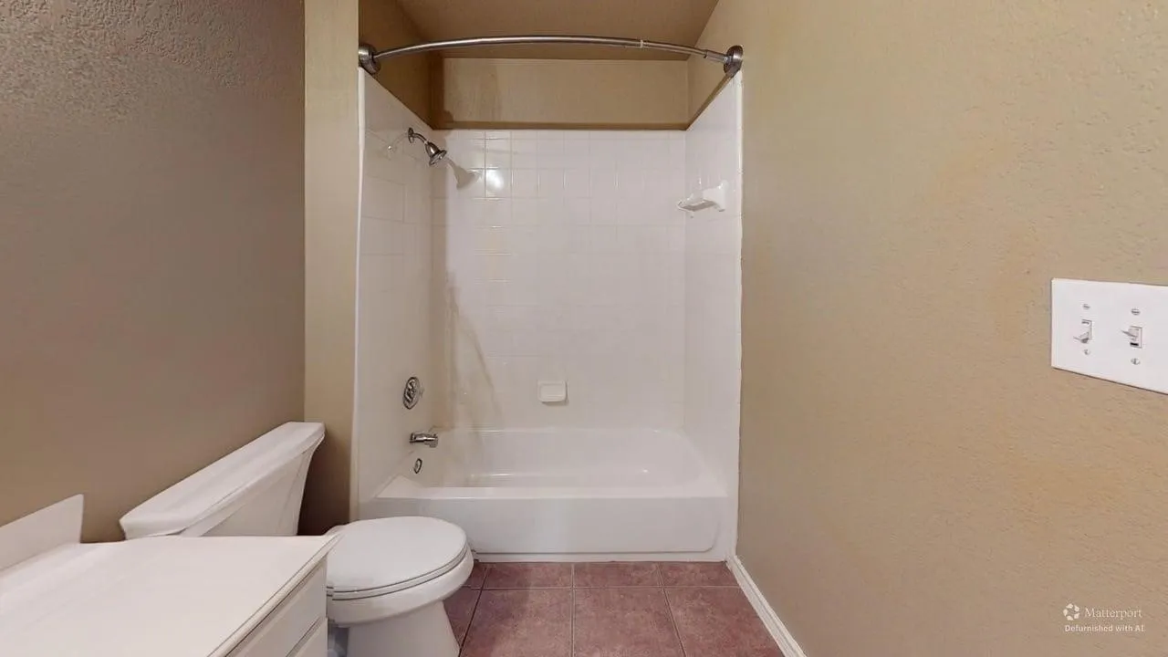 Integrated bathtub and shower combination with white tile surround, curved shower rod, and tiled flooring