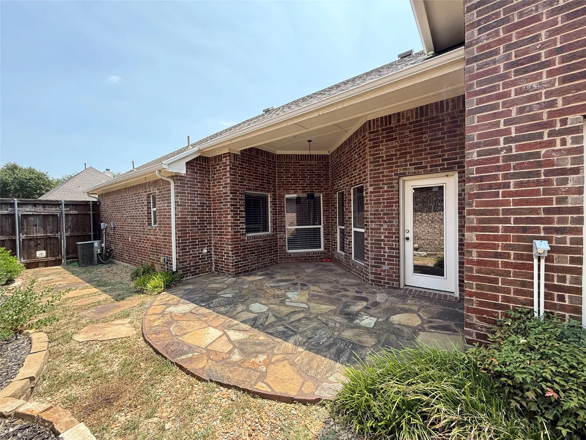 Covered patio featuring flagstone paving, brick exterior, and a white entry door