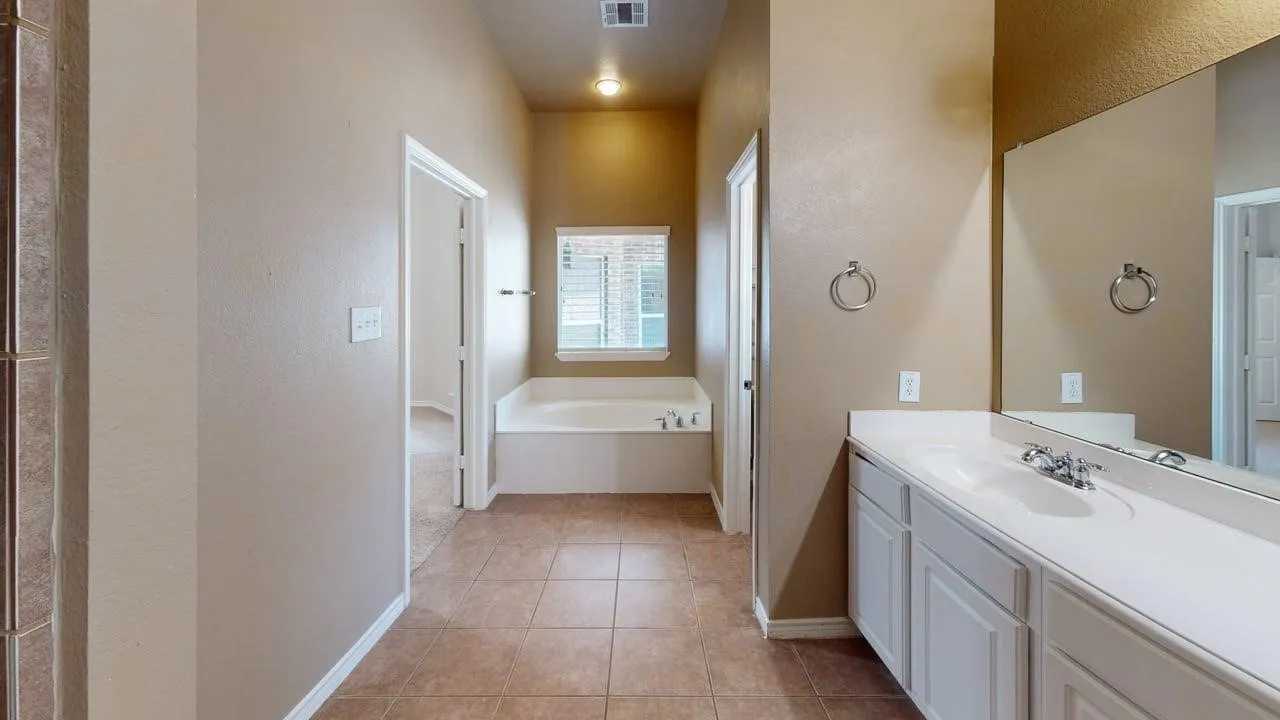 Tile flooring, built-in soaking tub, vanity with integrated sink, expansive vanity mirror, and overhead lighting