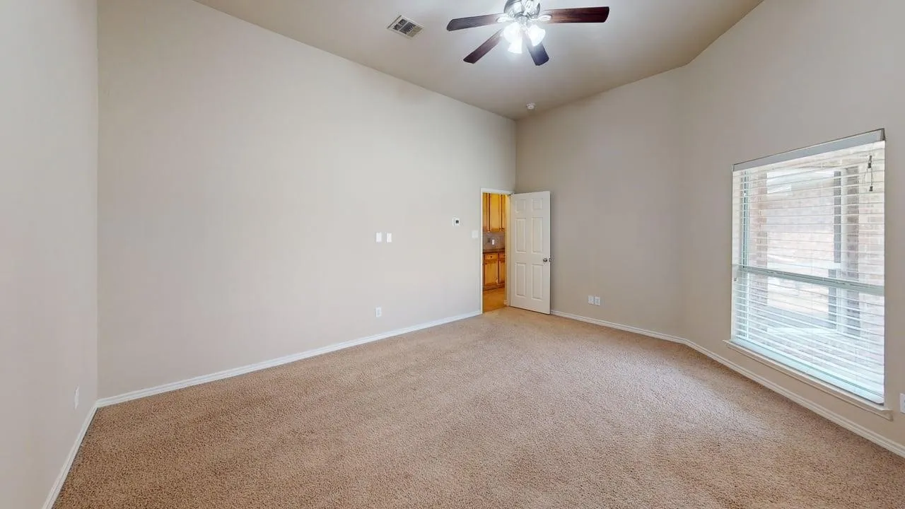 Carpeted room with a vaulted ceiling, ceiling fan, and a large window with blinds