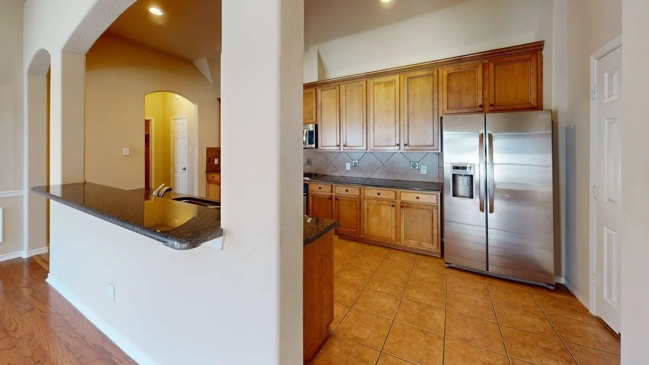 Spacious kitchen featuring warm wood cabinetry, stainless steel appliances, a tile backsplash, and tile flooring