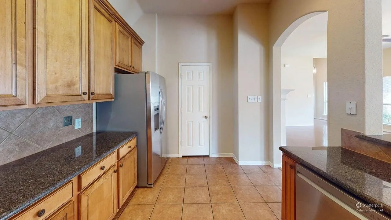Tile flooring, wood cabinetry, stainless steel appliances, granite countertops, and an arched doorway