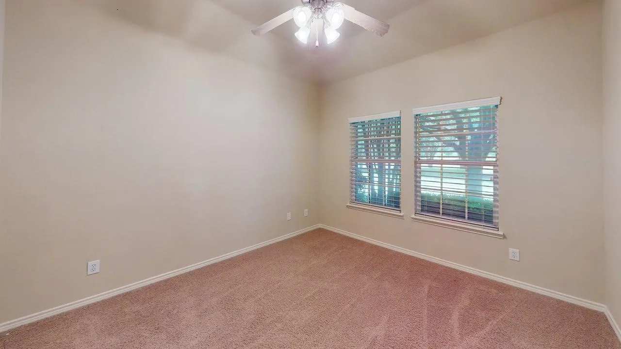 Carpeted flooring, neutral wall tones, two windows with blinds, and a ceiling fan with integrated lighting