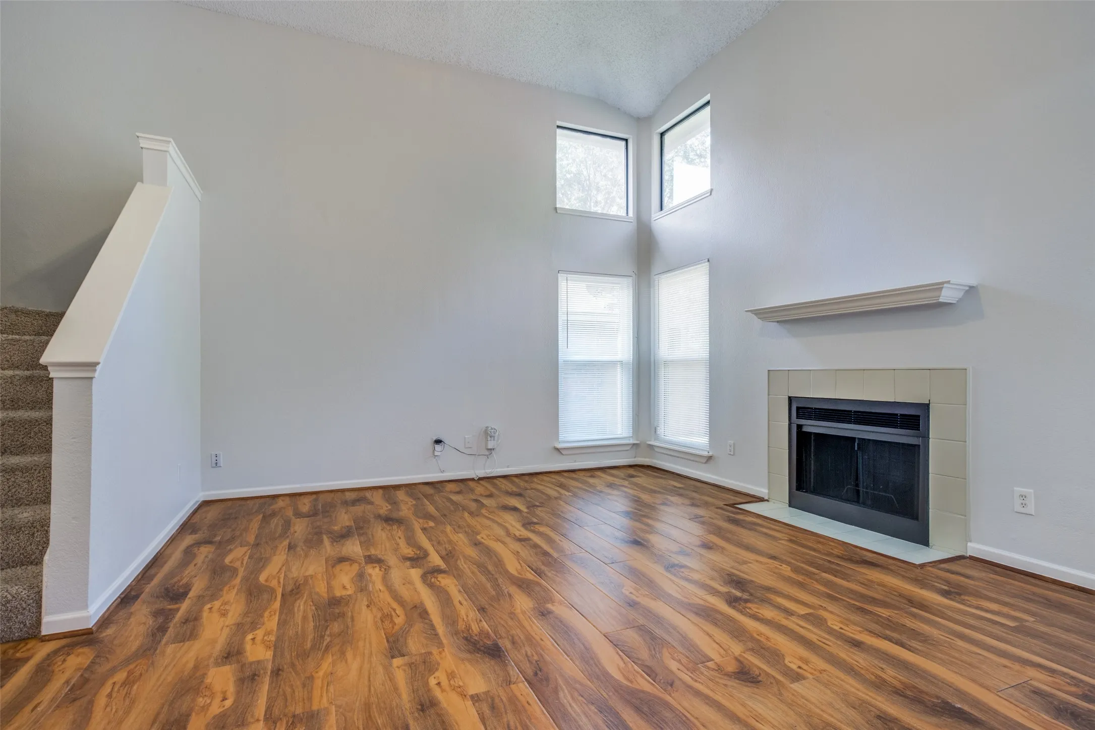 Vaulted ceiling, wood-finish flooring, tiled fireplace with mantel, multiple windows, and carpeted stairs