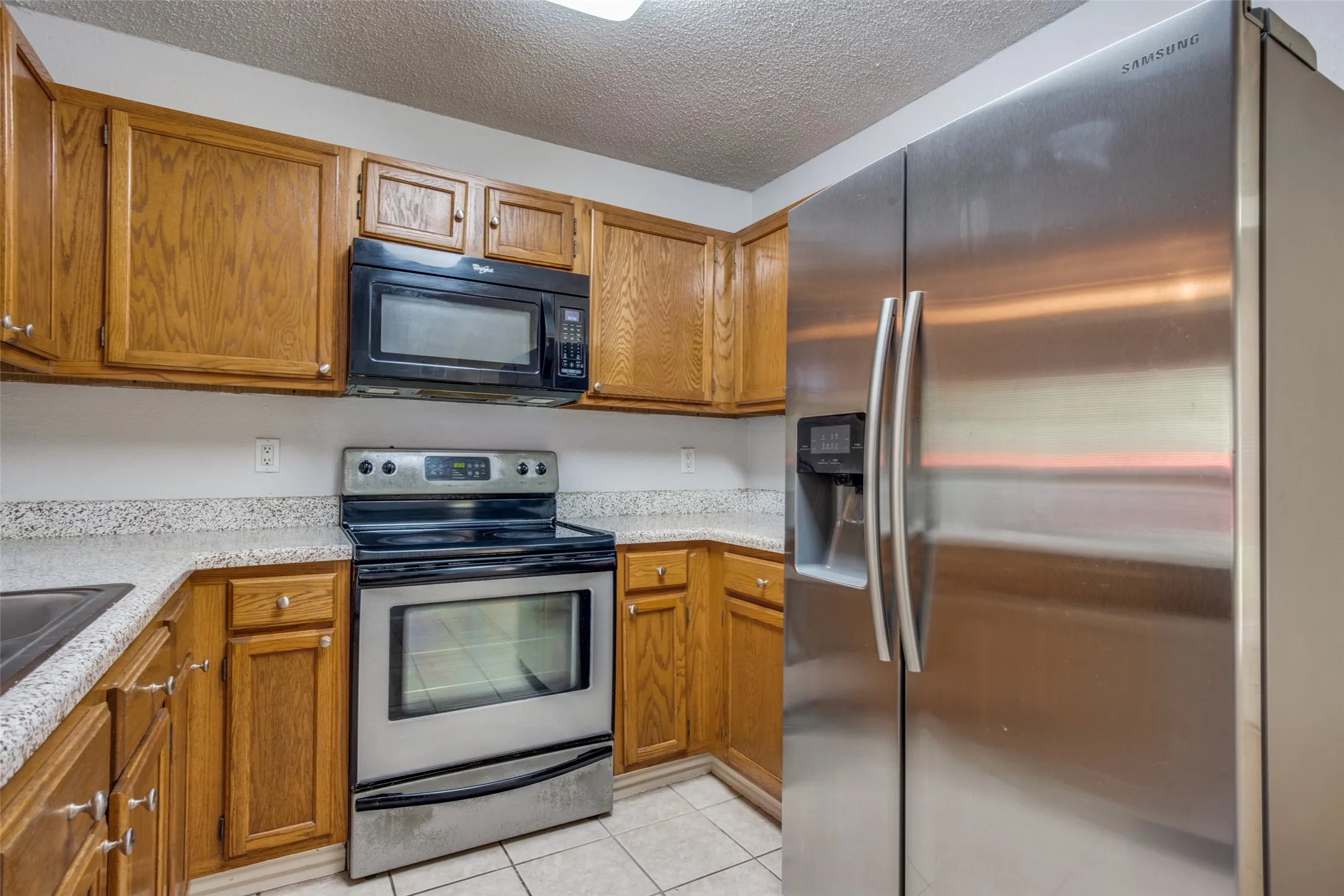 Kitchen featuring wood cabinetry, light-toned countertops, a stainless steel refrigerator, and a black and stainless steel range with an overhead microwave