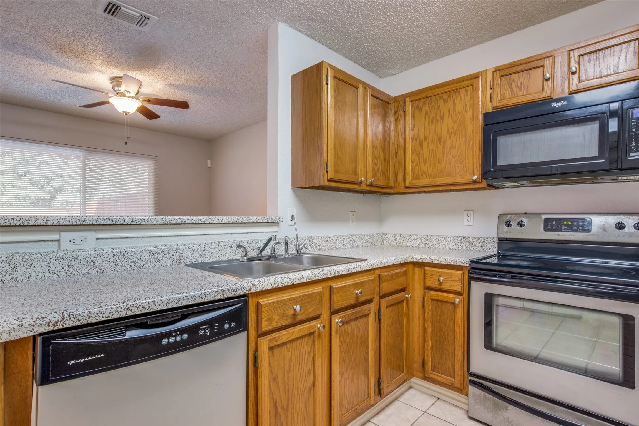 Kitchen featuring wood cabinetry, light-toned countertops, a stainless steel dishwasher, and a stainless steel range with an overhead microwave