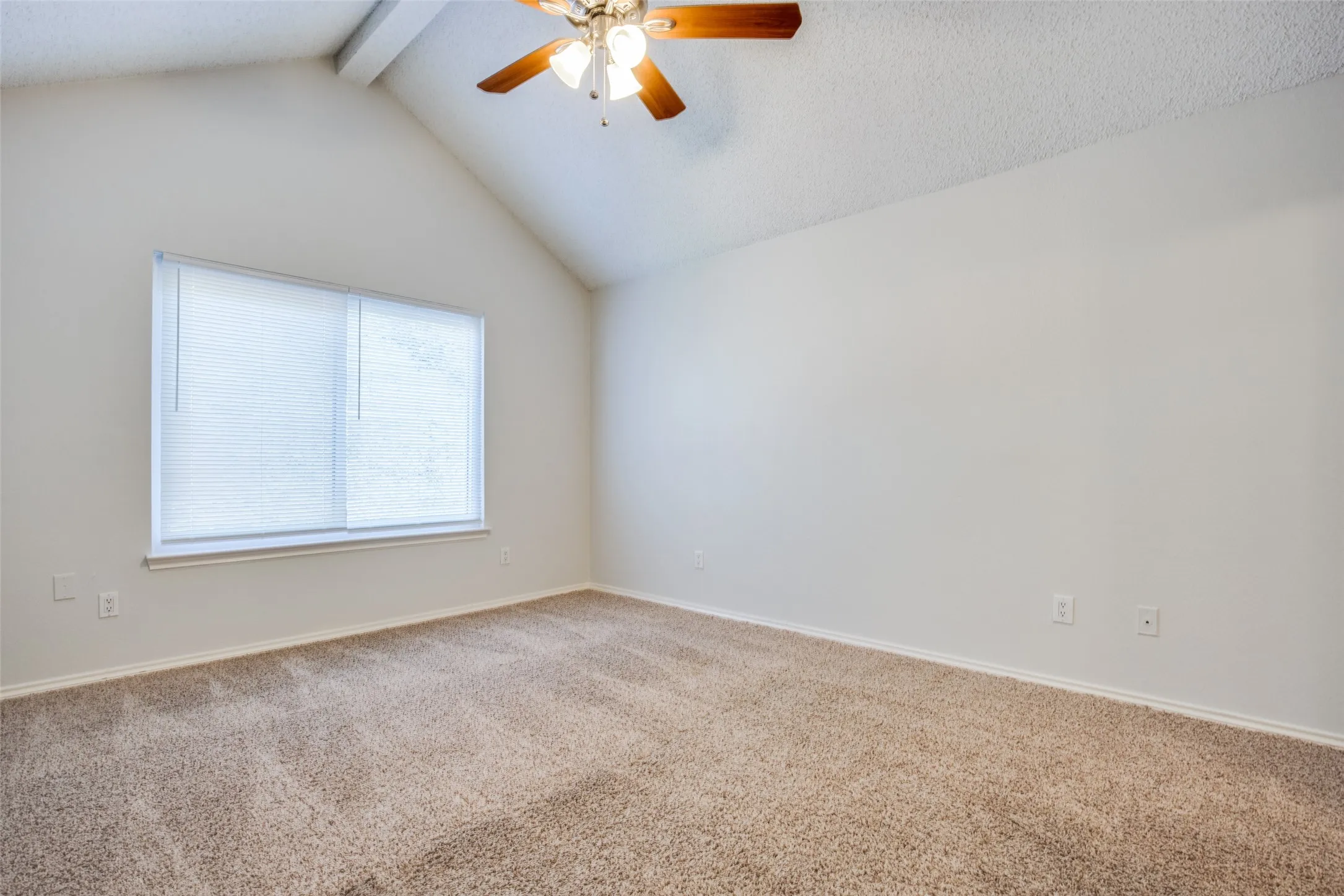 Vaulted ceiling with a wood-finish ceiling fan, neutral-toned carpeting, and a window with blinds