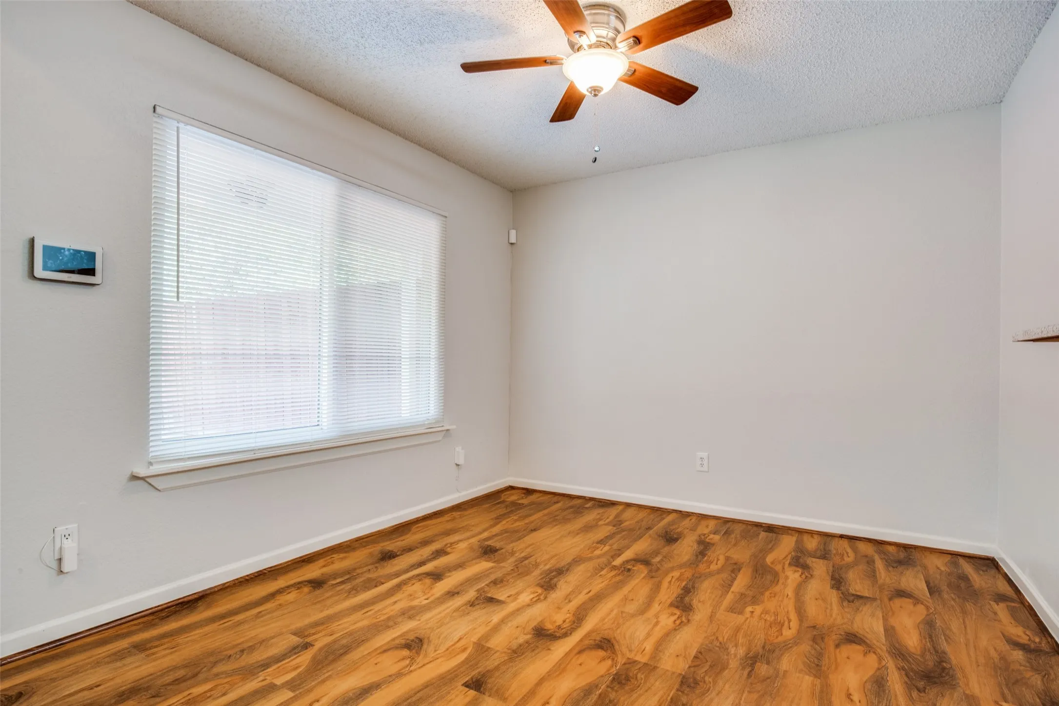 Bright, light-filled bedroom featuring hardwood flooring, a ceiling fan with integrated lighting, and large window with horizontal blinds allowing abundant natural light