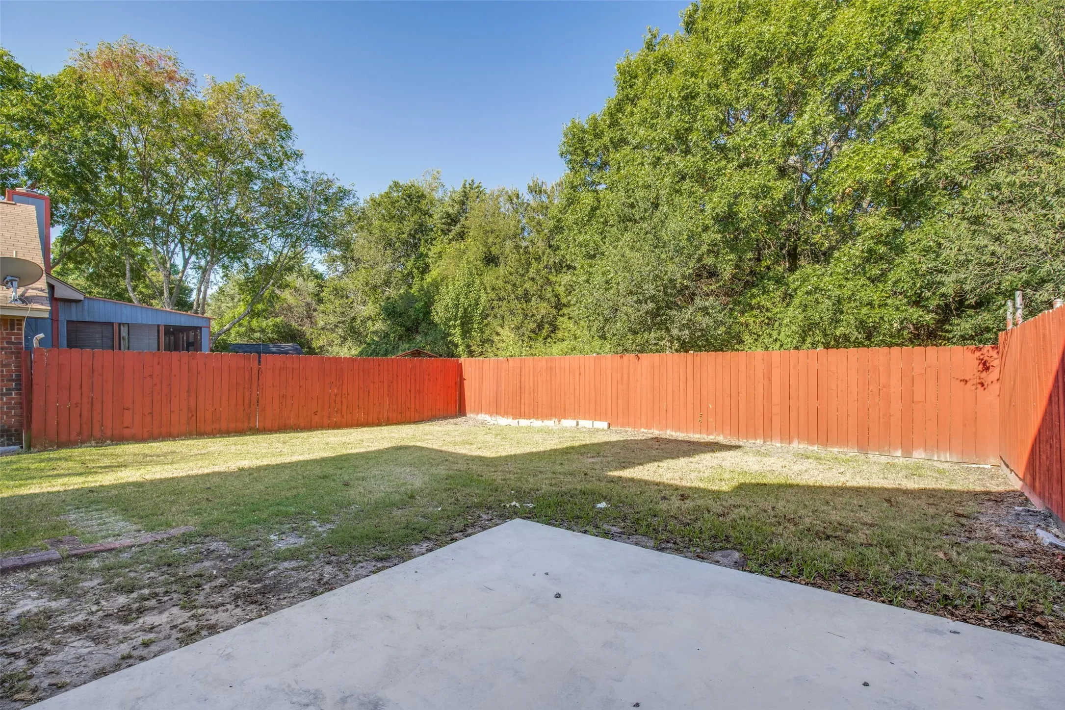 Private backyard featuring a concrete patio, wood privacy fencing, and mature perimeter trees