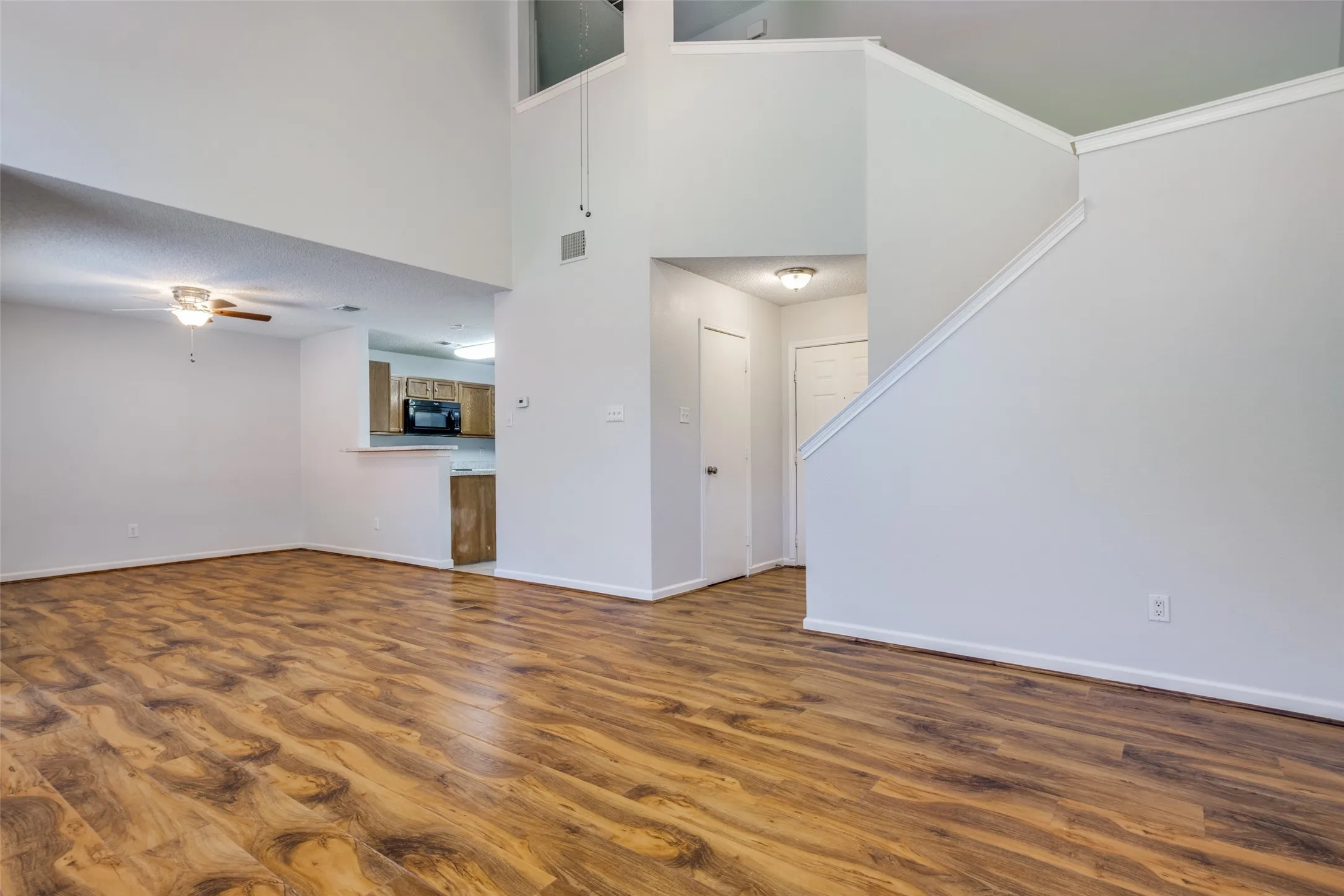 Expansive living area featuring wood-finish flooring, high ceilings, and a ceiling fan with integrated lighting