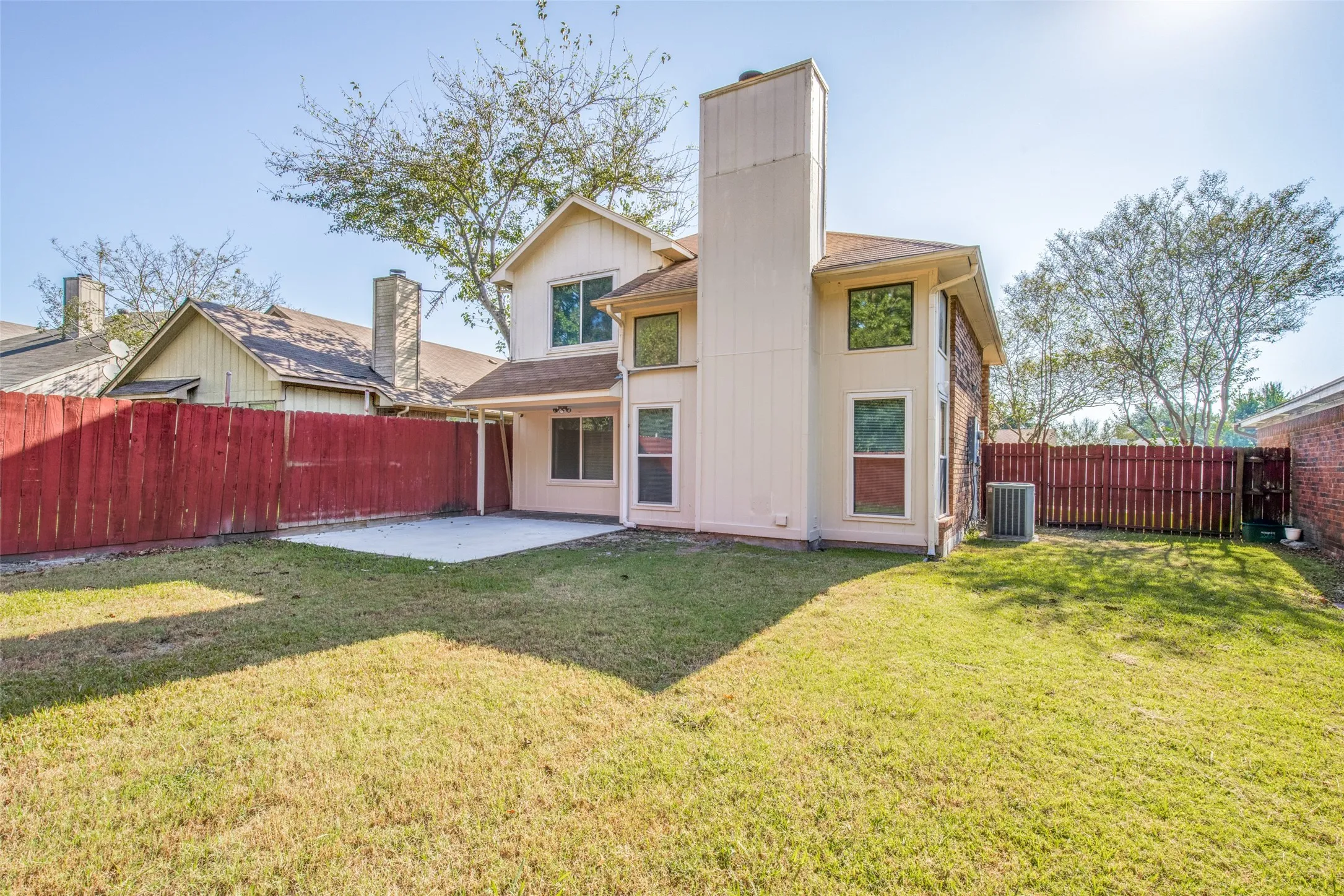 Expansive backyard featuring a concrete patio, wood fencing, and mature trees