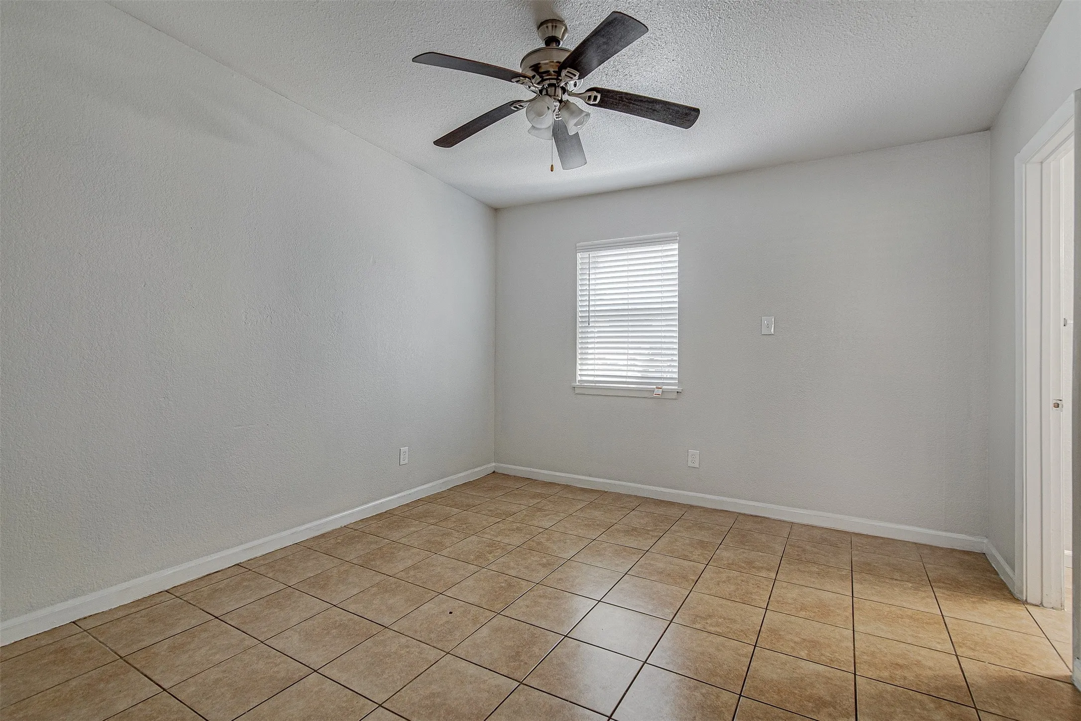 Neutral-toned walls with a textured finish, ceiling fan, window with blinds, and tile flooring