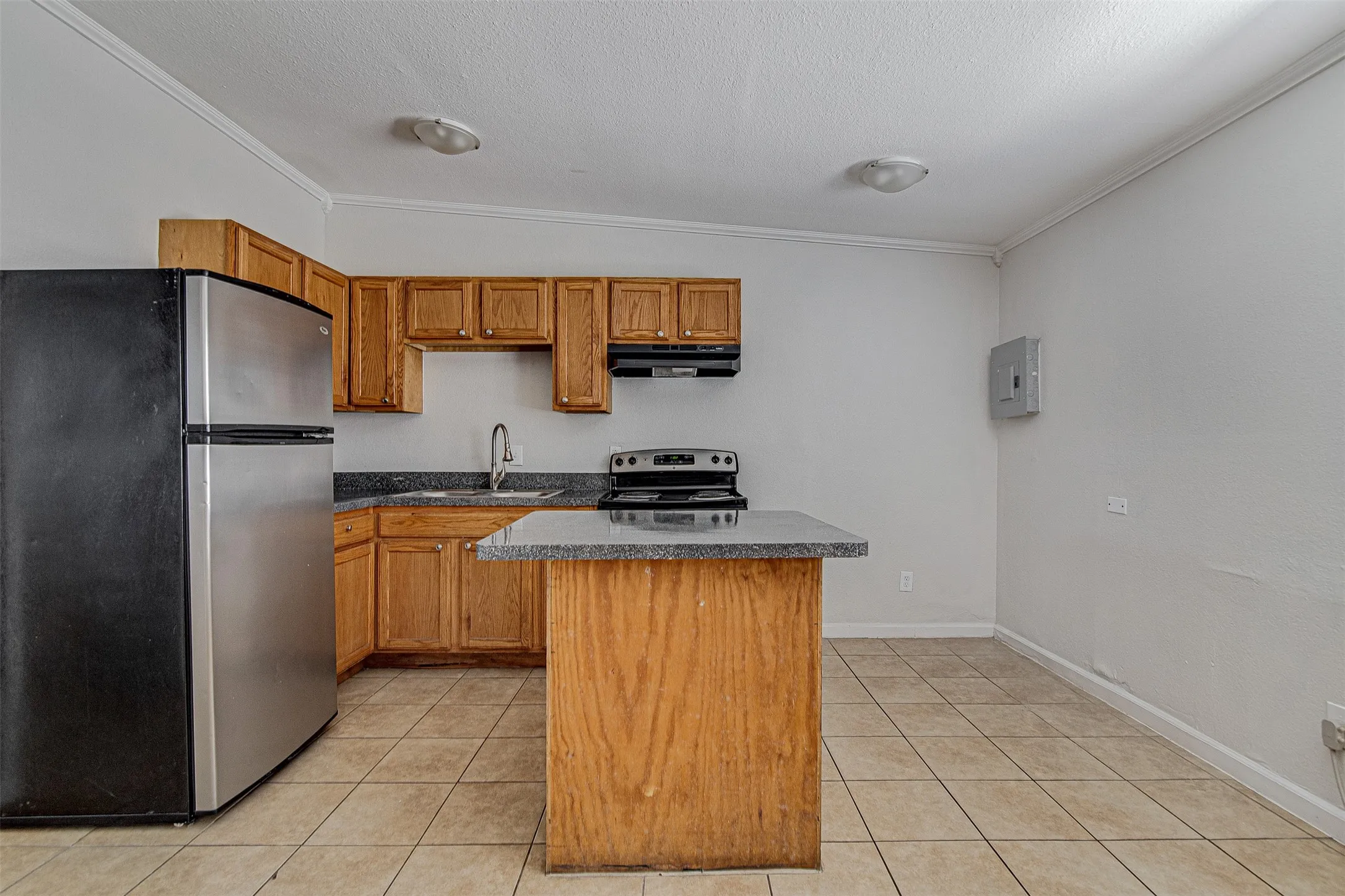 Kitchen featuring wood cabinetry, dark countertops, tiled flooring, stainless steel refrigerator, and a kitchen island
